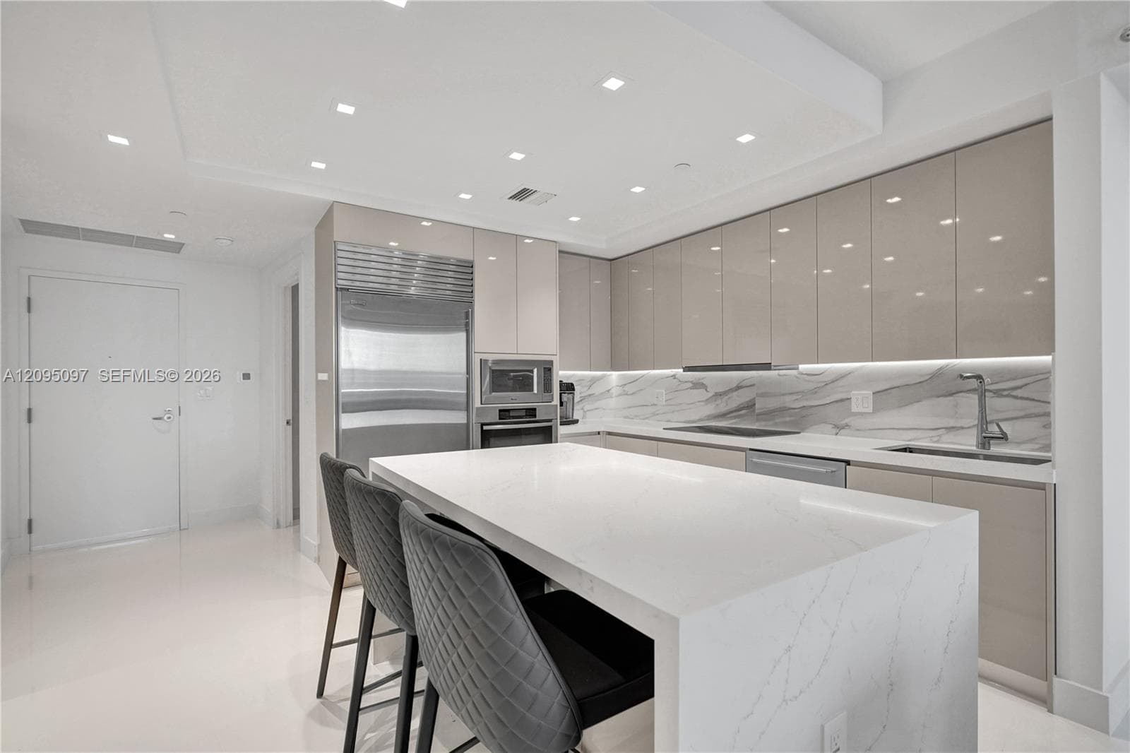 Contemporary kitchen featuring high-gloss cabinetry, a waterfall-edge quartz island, under-cabinet lighting, integrated stainless steel appliances, and stone-finish backsplash