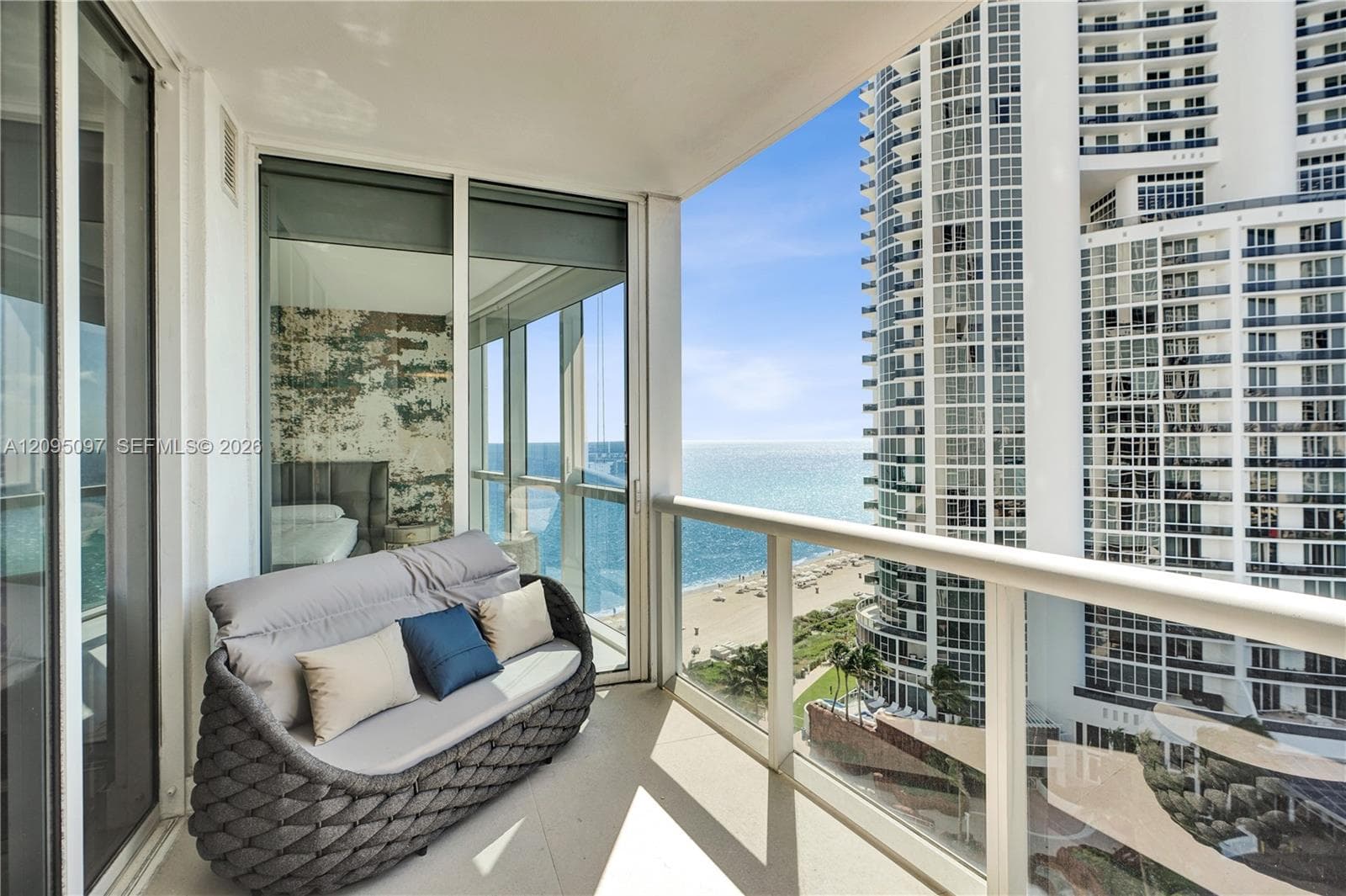 Covered private balcony featuring glass panel railings, floor-to-ceiling sliding glass doors, and panoramic ocean and coastline exposure