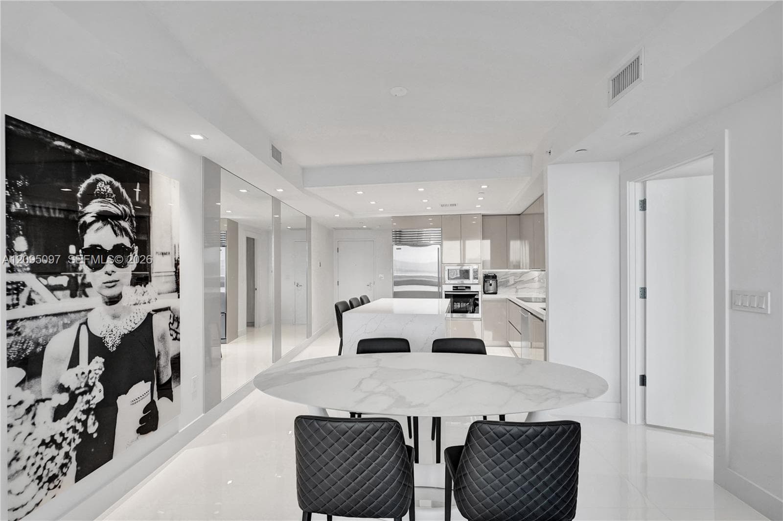 Open-concept kitchen featuring high-gloss cabinetry, a central island with stone-finish countertops, stainless steel appliances, recessed lighting, and polished stone flooring