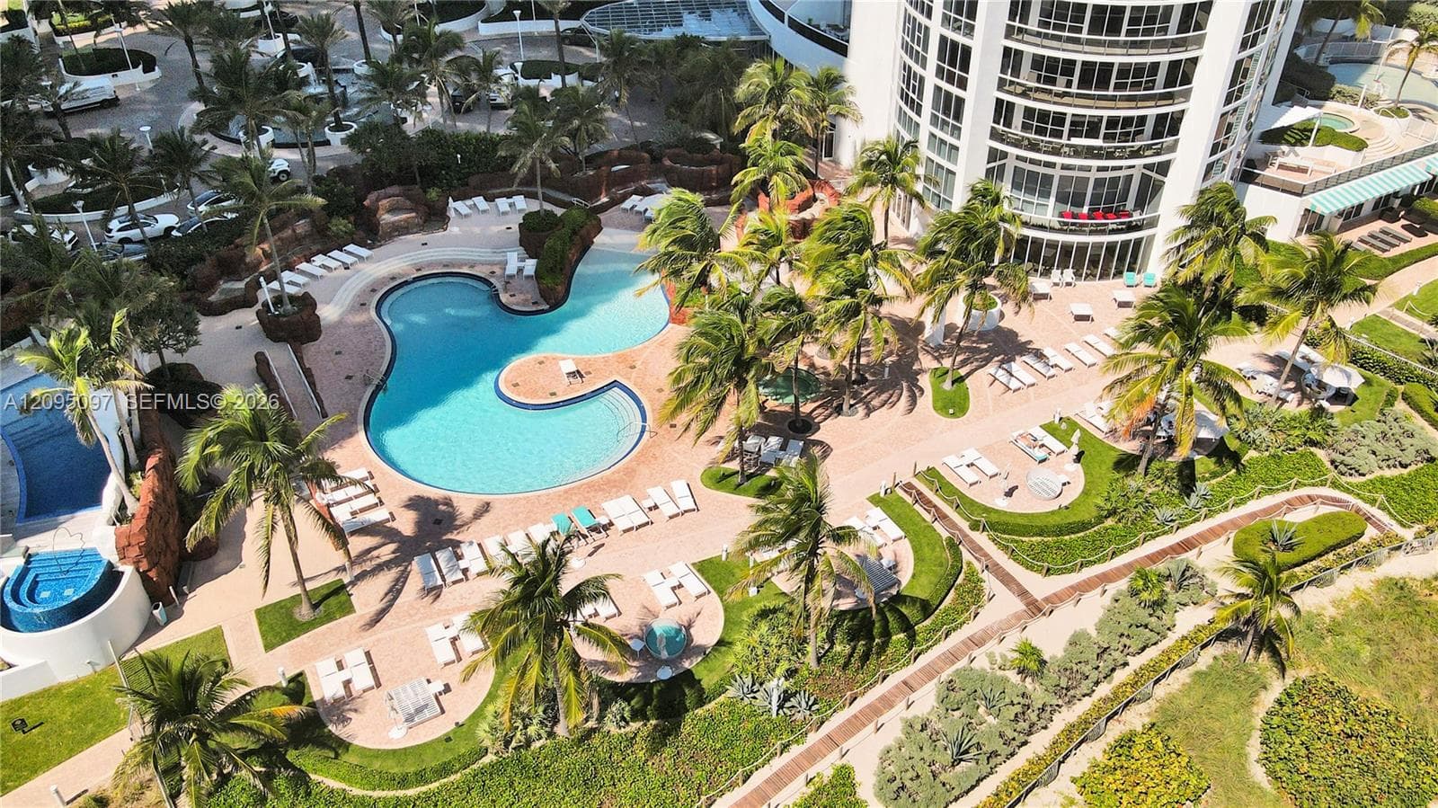 Aerial view of a high-rise building featuring a free-form swimming pool, integrated spa, paved sun deck, and tropical landscaping