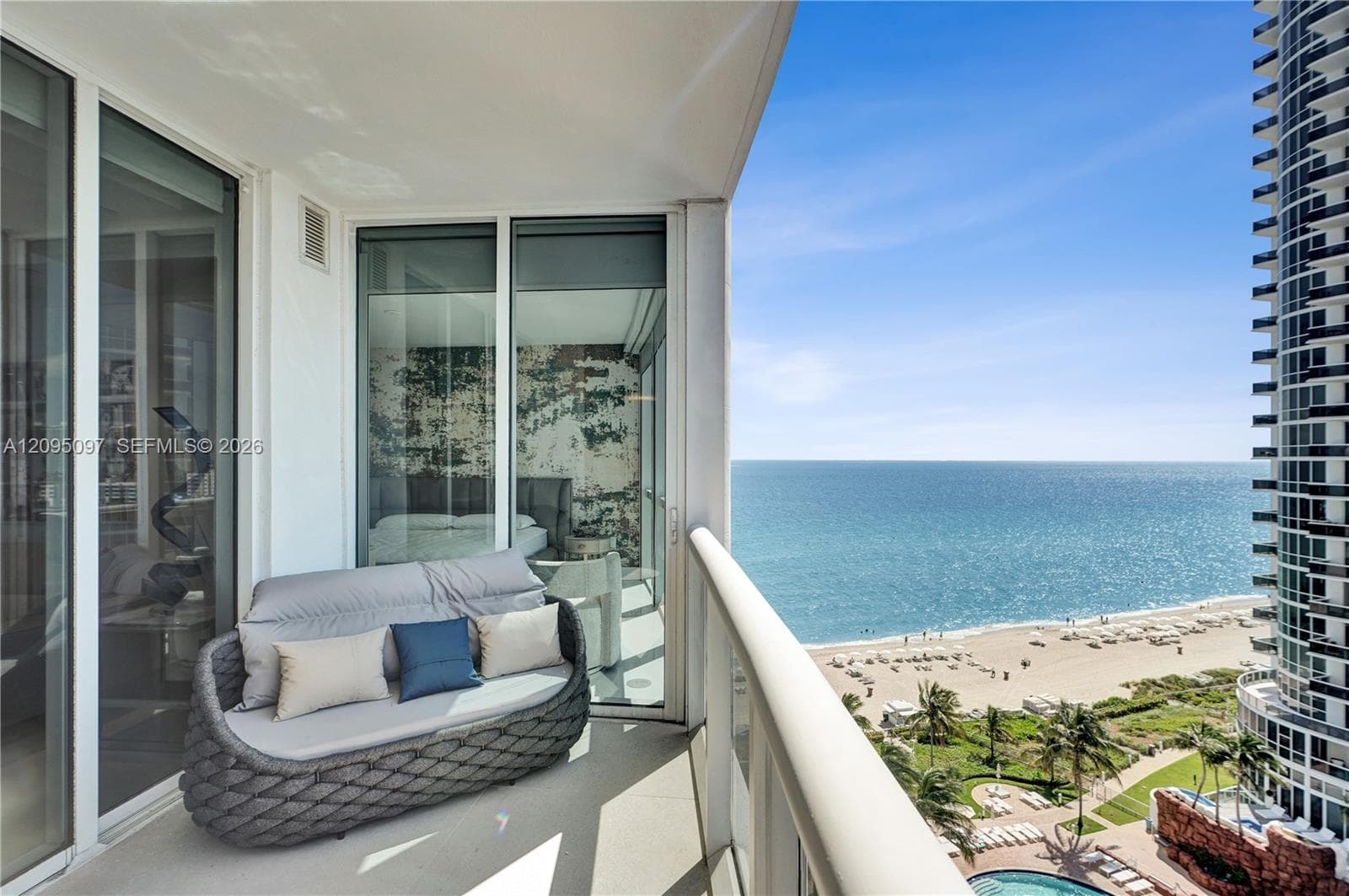 Private balcony with full-height glass railing, floor-to-ceiling sliding glass doors, and panoramic oceanfront exposure