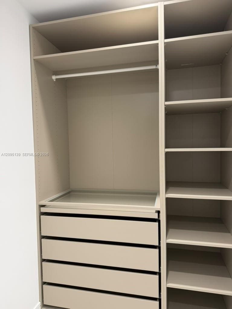 Built-in closet system featuring neutral-toned cabinetry, four smooth-glide storage drawers, a glass-topped dresser surface, adjustable shelving, and a metal hanging rod