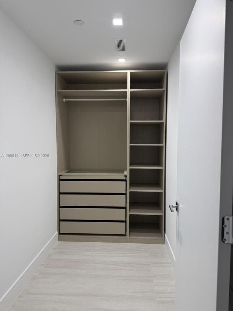 Built-in storage system featuring a taupe finish, four deep drawers, open shelving, and a hanging rod, complemented by wood-finish flooring and recessed ceiling lighting