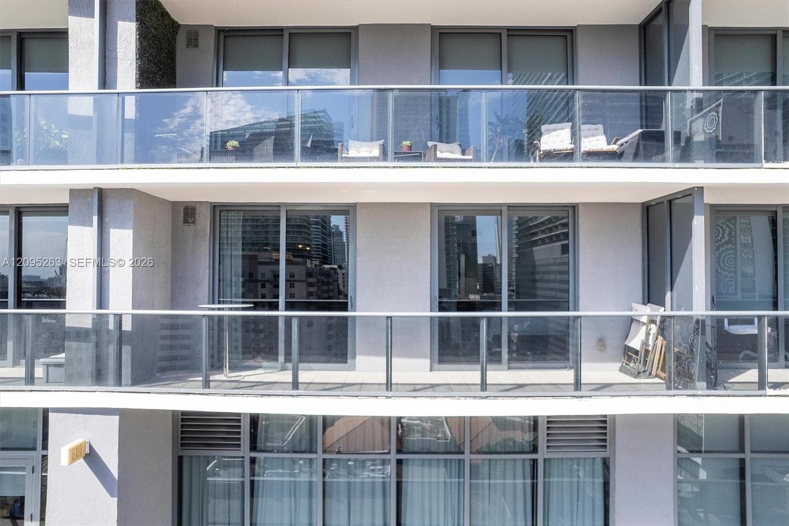 Multi-story exterior featuring expansive private balconies with glass railings and floor-to-ceiling sliding glass doors