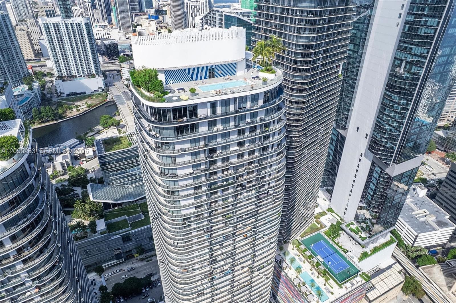 High-rise building featuring a rooftop swimming pool, landscaped terrace, wrap-around balconies, and a multi-level recreational deck with an outdoor court