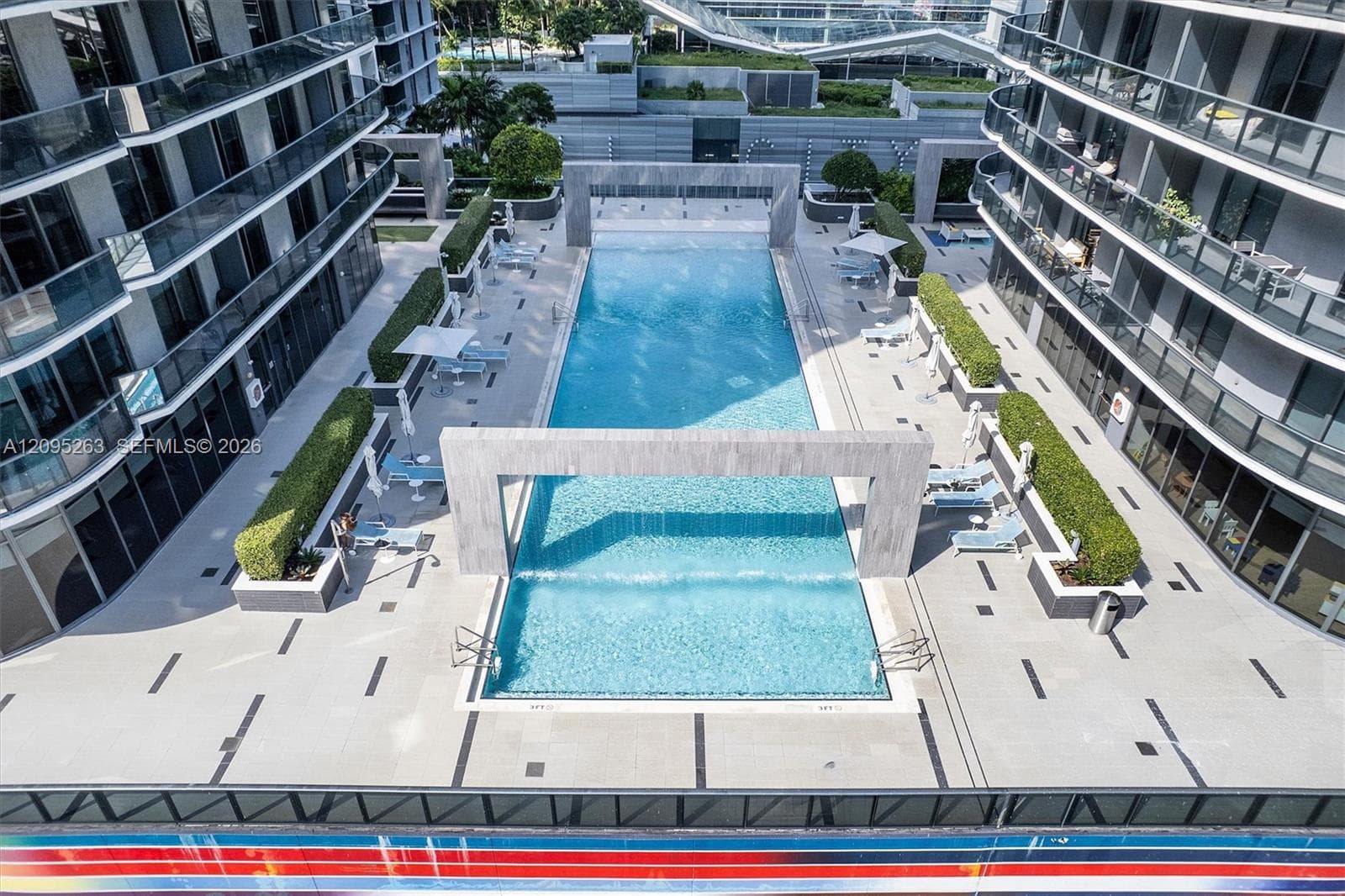 Resort-style lap pool featuring stone-clad water features, integrated sun shelf, sprawling paved deck, and structured shrubbery