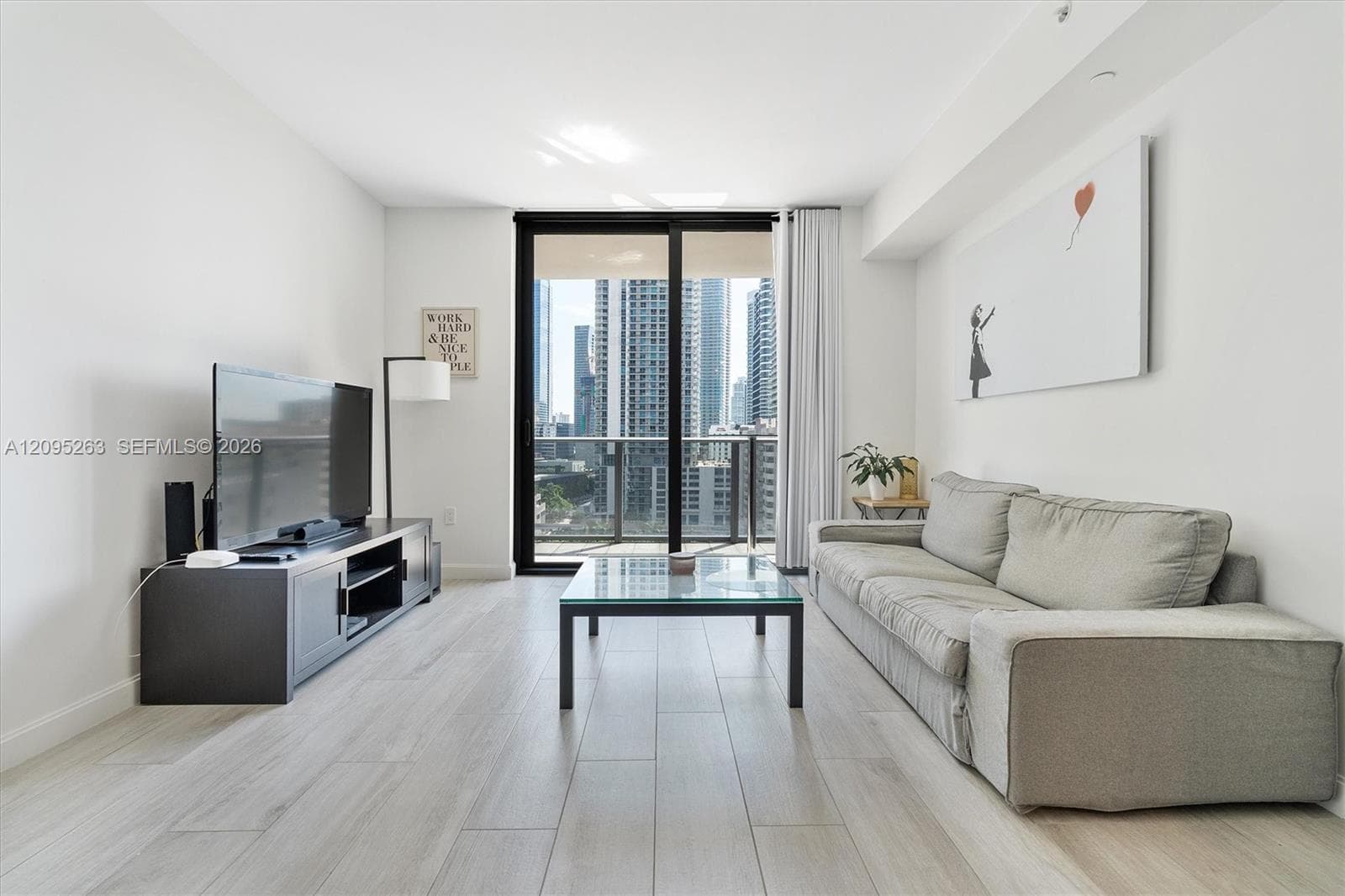 Living area featuring wood-finish flooring, floor-to-ceiling sliding glass doors, and a private balcony with metal railing