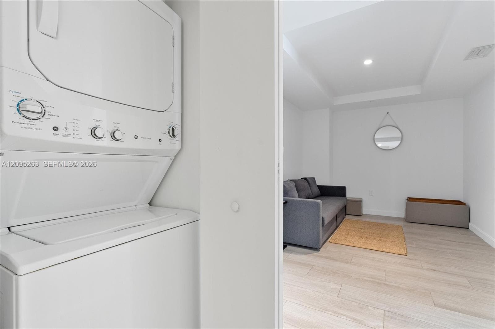 Stacked laundry unit featuring a white finish, wood-finish flooring, and recessed ceiling lighting