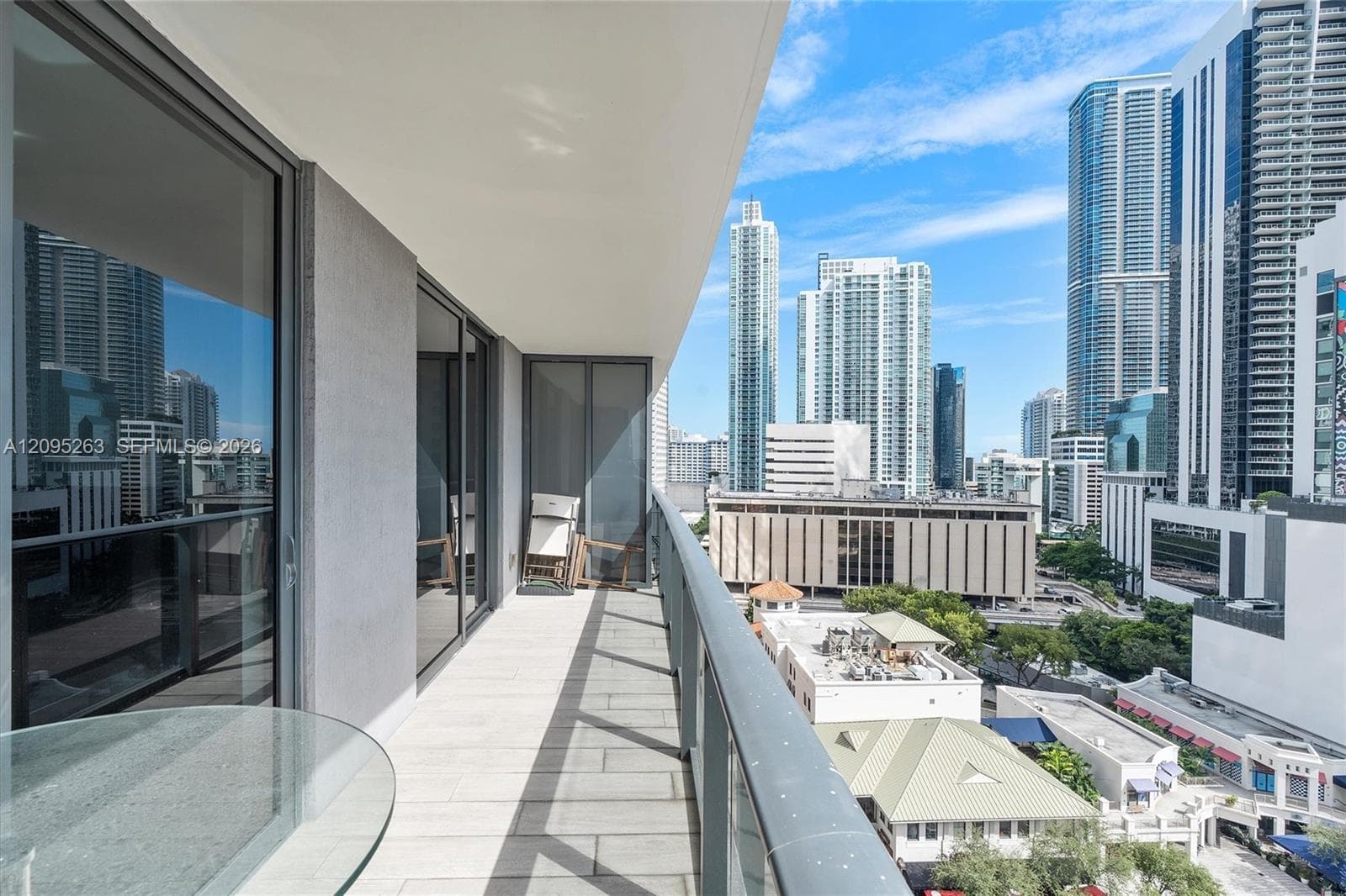Covered balcony featuring tile flooring, full-height sliding glass doors, and a glass-paneled railing overlooking the cityscape
