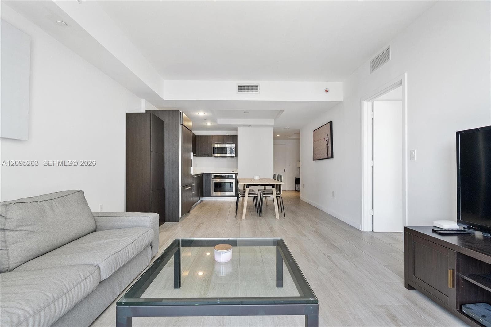 Open-concept interior featuring light-tone wood-finish flooring, dark cabinetry, stainless steel kitchen appliances, and recessed lighting