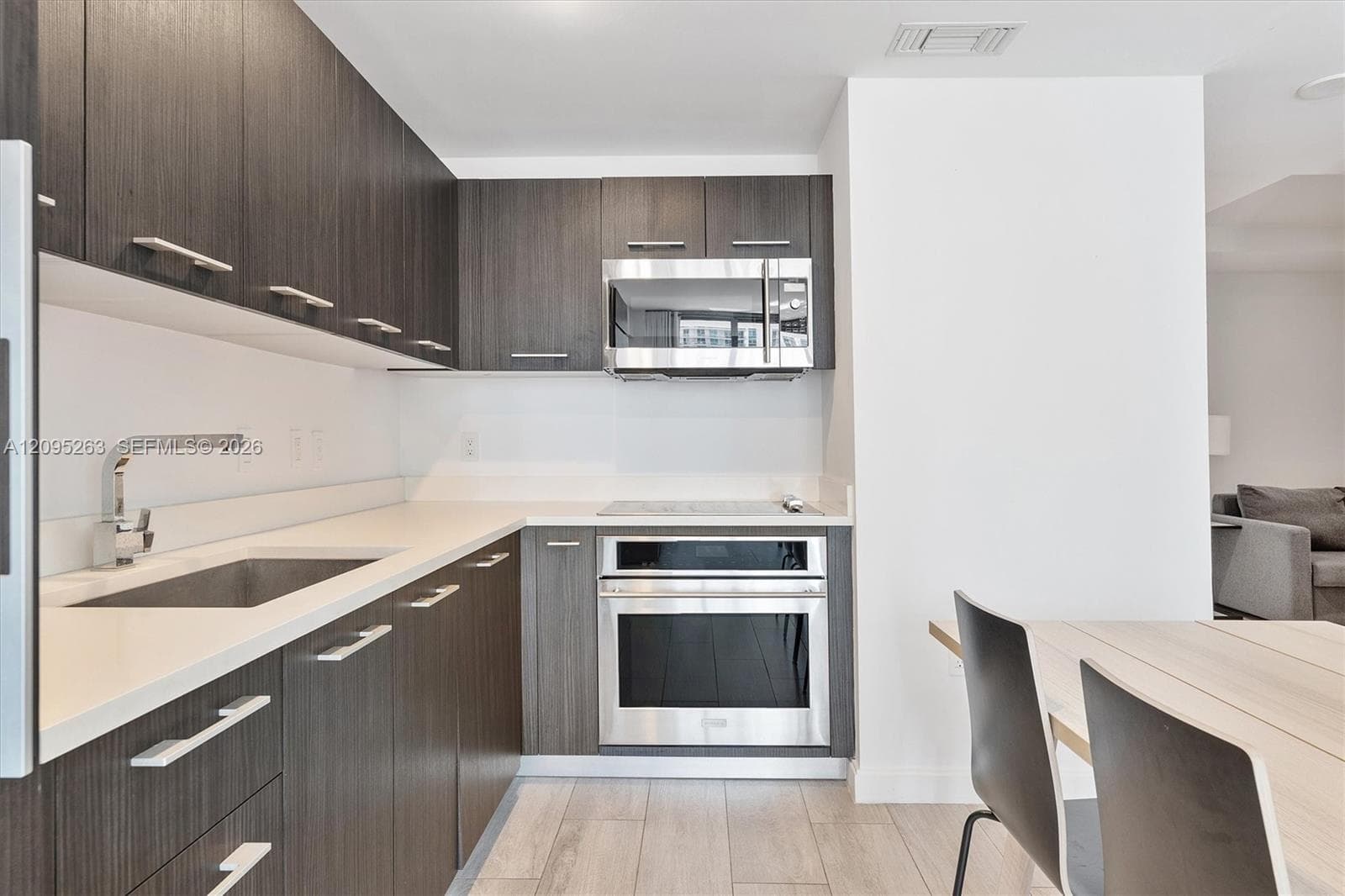 Kitchen featuring dark-toned cabinetry, light-colored countertops, stainless steel appliances, and wood-finish flooring