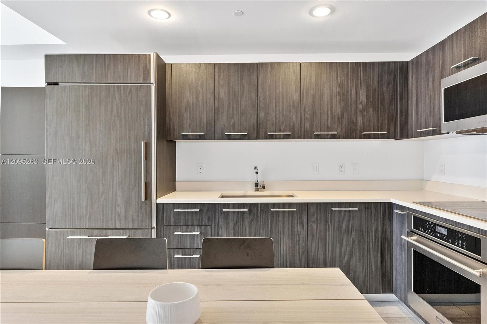 Modern kitchen featuring dark wood-finish cabinetry, integrated panel-ready refrigerator, solid-surface countertops, and stainless steel built-in oven and microwave