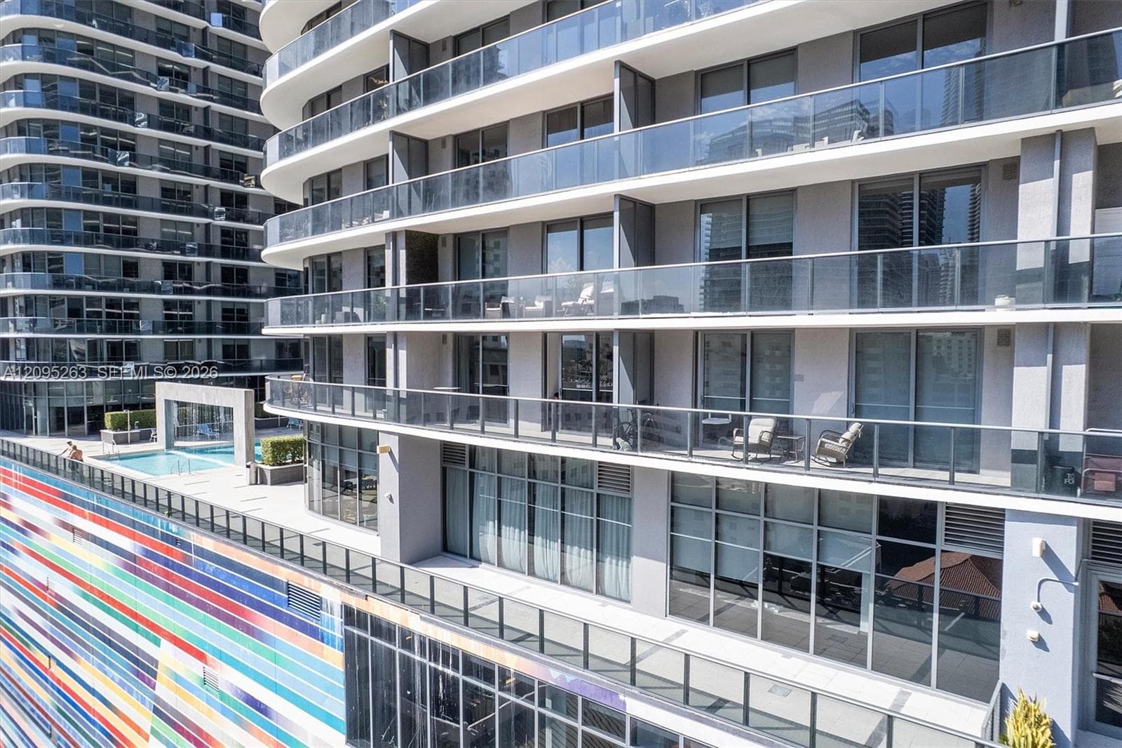 High-rise exterior featuring extensive glass-panel balconies, floor-to-ceiling windows, and multi-colored linear facade detailing