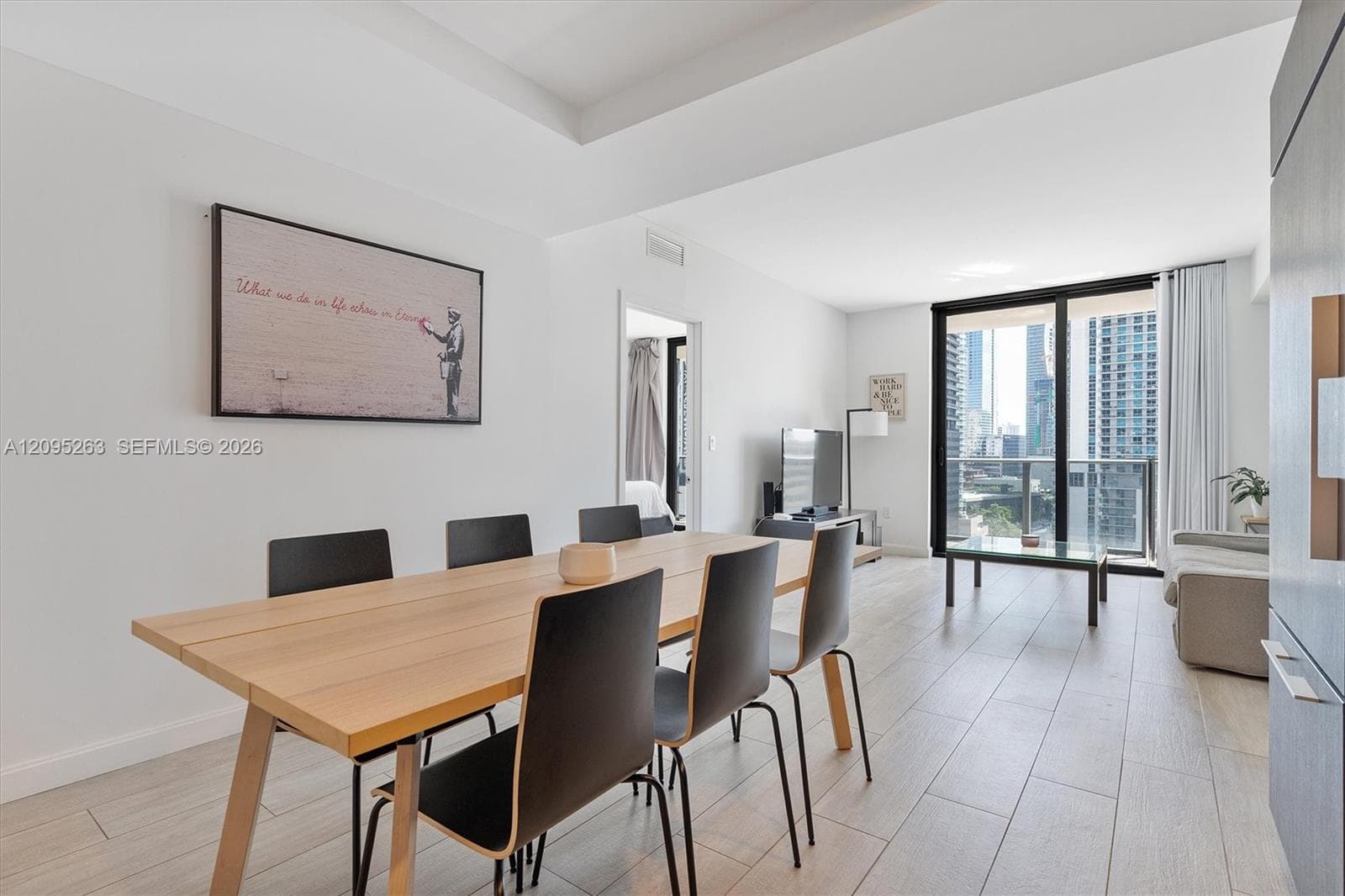 Open-concept living space featuring wood-finish tile flooring, recessed tray ceiling, floor-to-ceiling glass sliding doors, and a private balcony