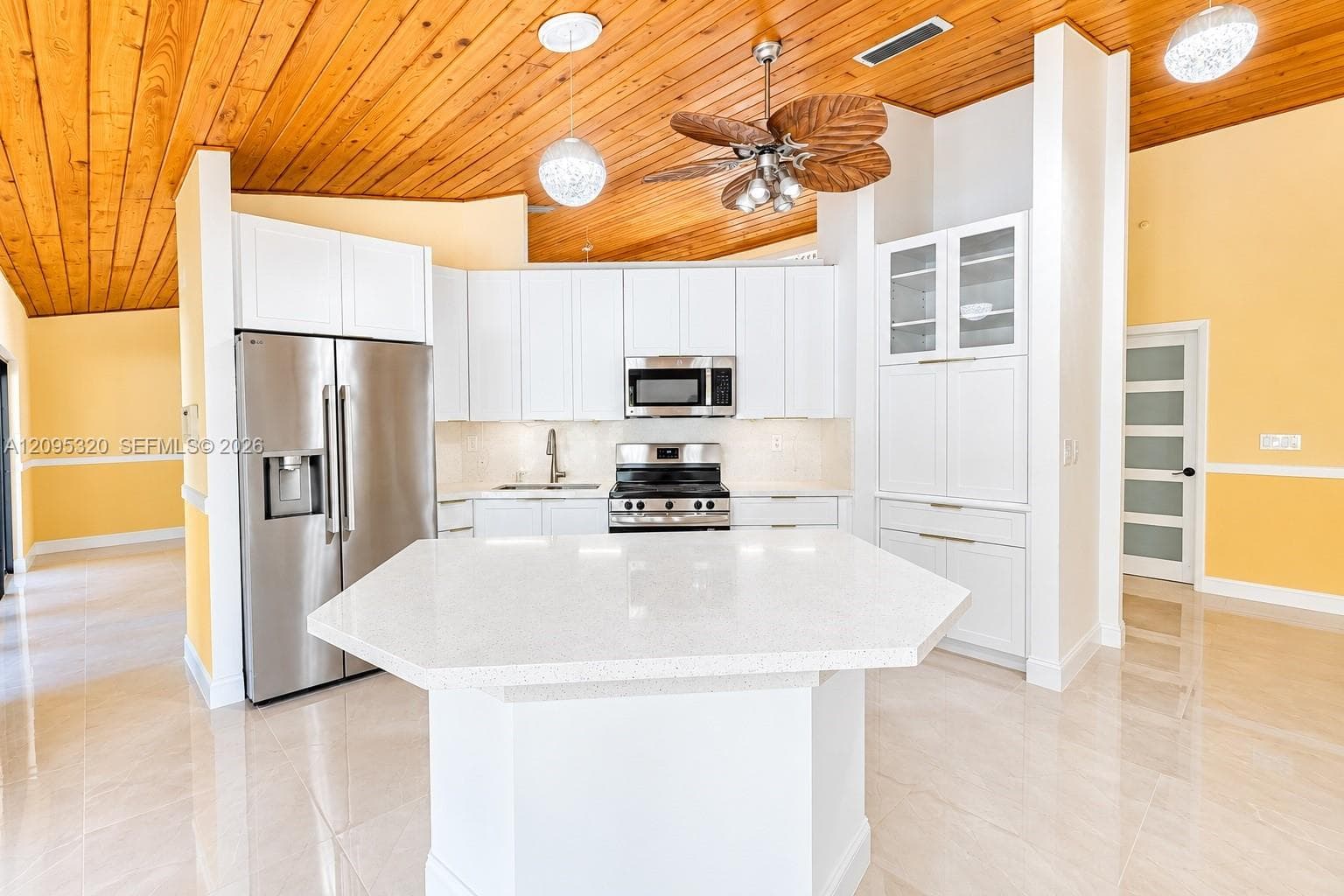 White cabinetry with stainless steel appliances and a hexagonal island featuring a light-toned countertop