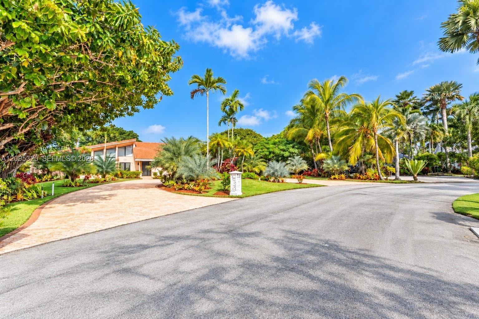 Paved driveway leading to the residence, vibrant green lawn, mature trees, and established landscaping