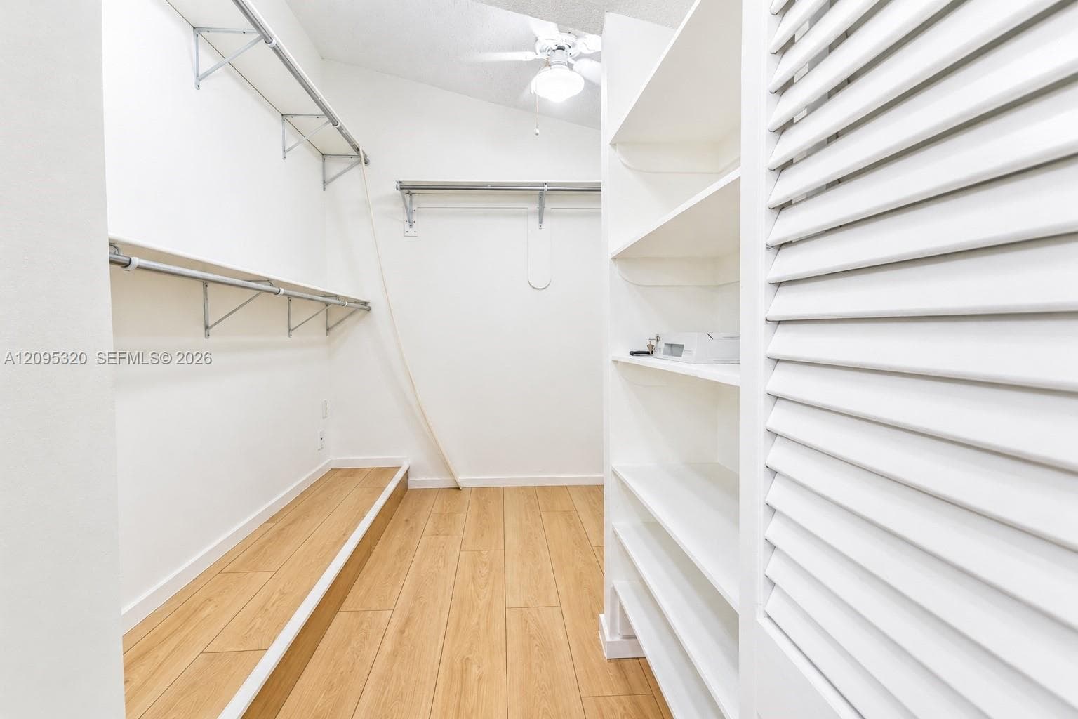 Vaulted ceiling with a ceiling fan, wood-finish flooring, built-in shelving, and louvered door