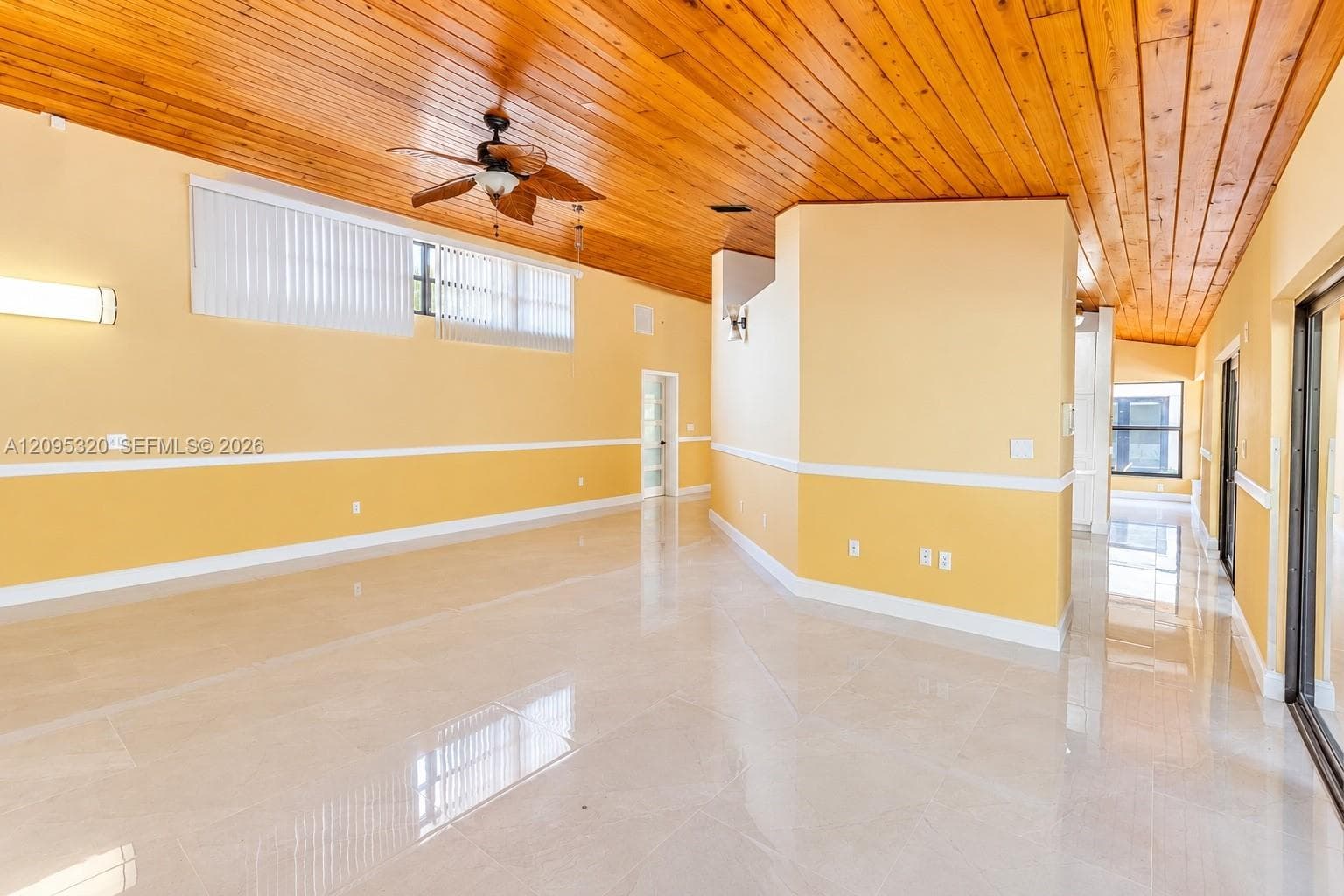 Vaulted wood-plank ceiling, ceiling fan with integrated lighting, polished tile flooring, and wall-mounted lighting fixtures