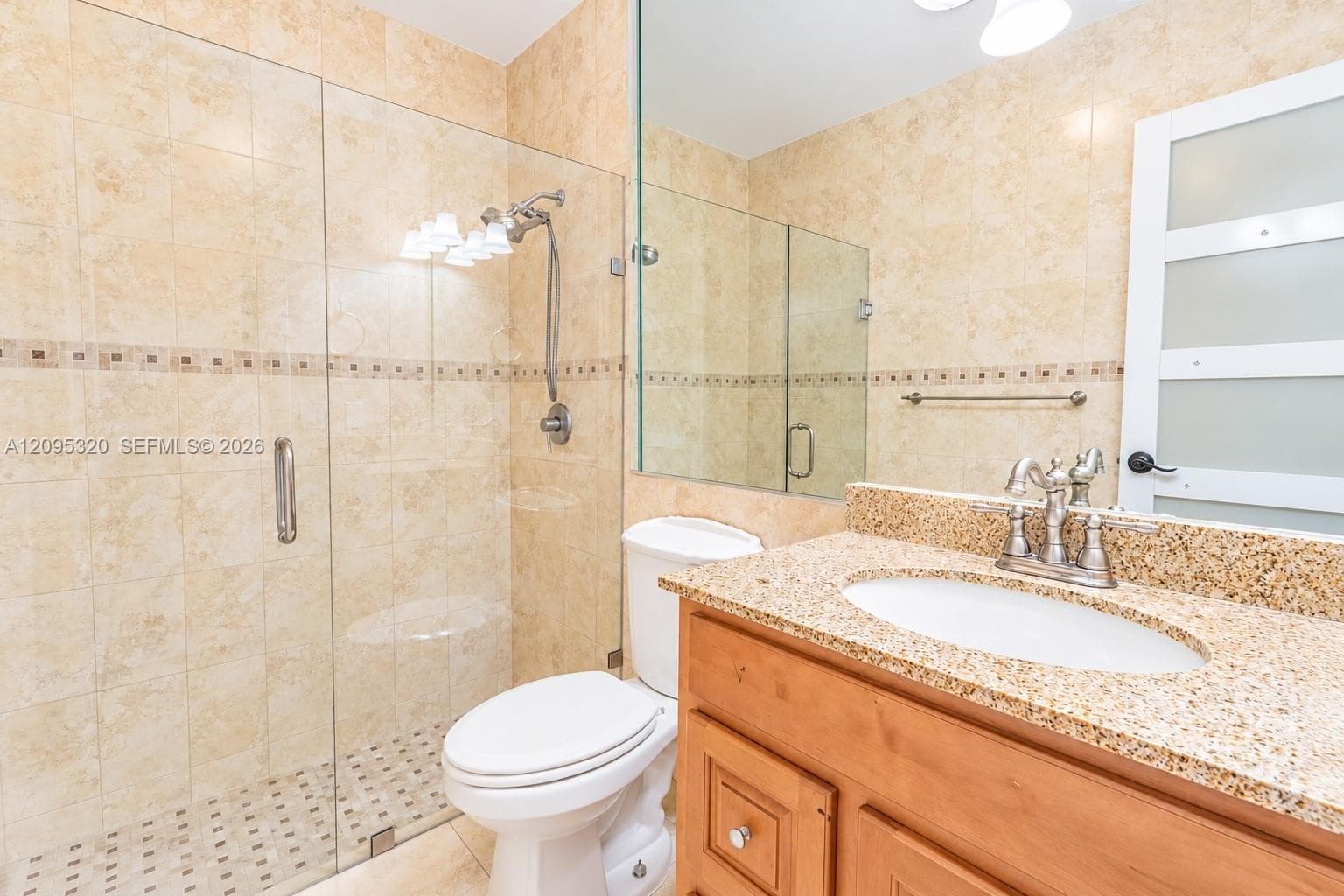 Glass-enclosed shower with full-height tile surround, wood-finish vanity with an undermount sink, and speckled countertop