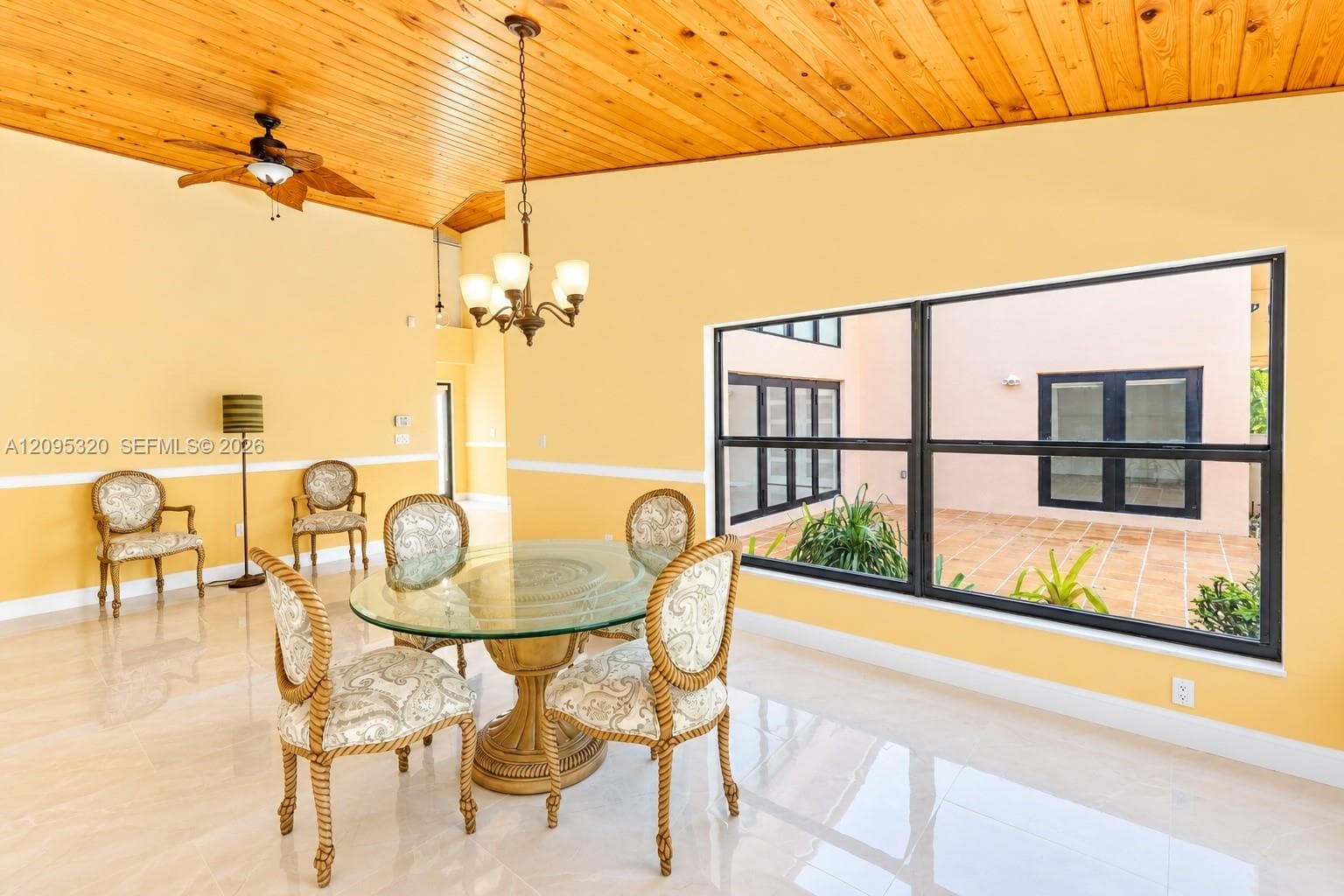 Vaulted wood-paneled ceiling, chandelier, ceiling fan, large fixed window, and polished tile flooring