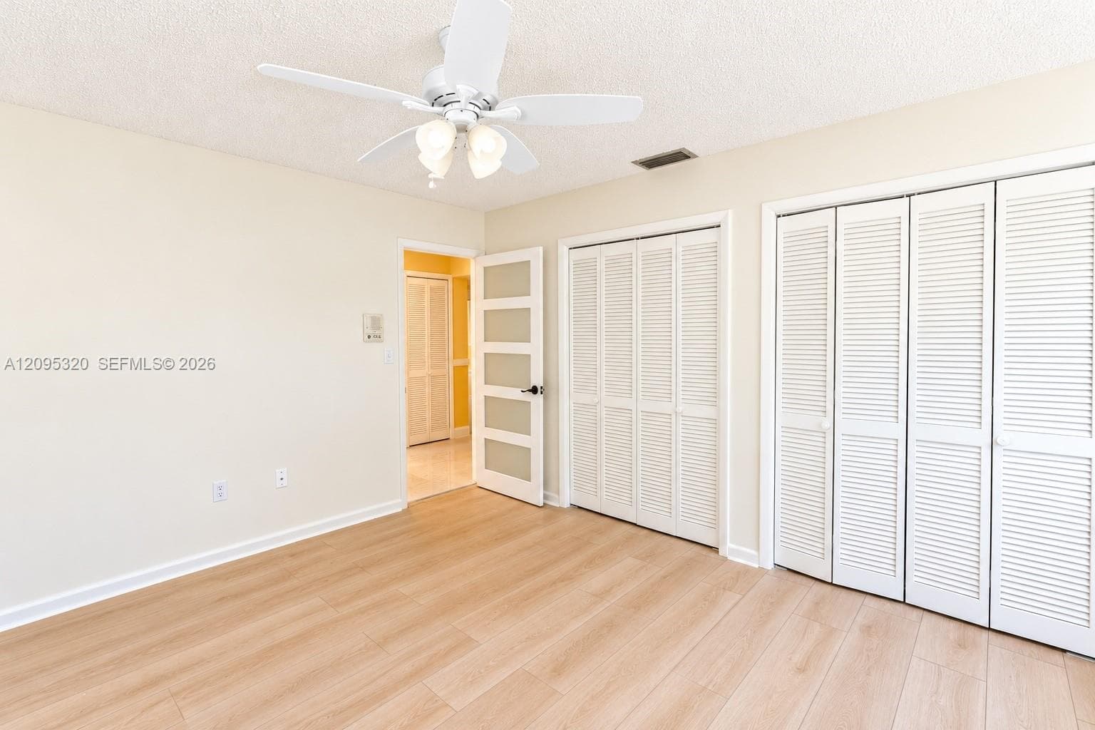 Light wood-finish flooring, white louvered bifold closet doors, and a ceiling fan with integrated lighting