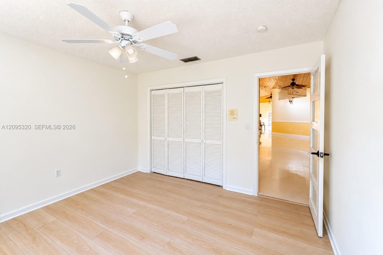 Wood-finish flooring, white bi-fold closet doors, ceiling fan with integrated lighting, and a white interior door with black hardware
