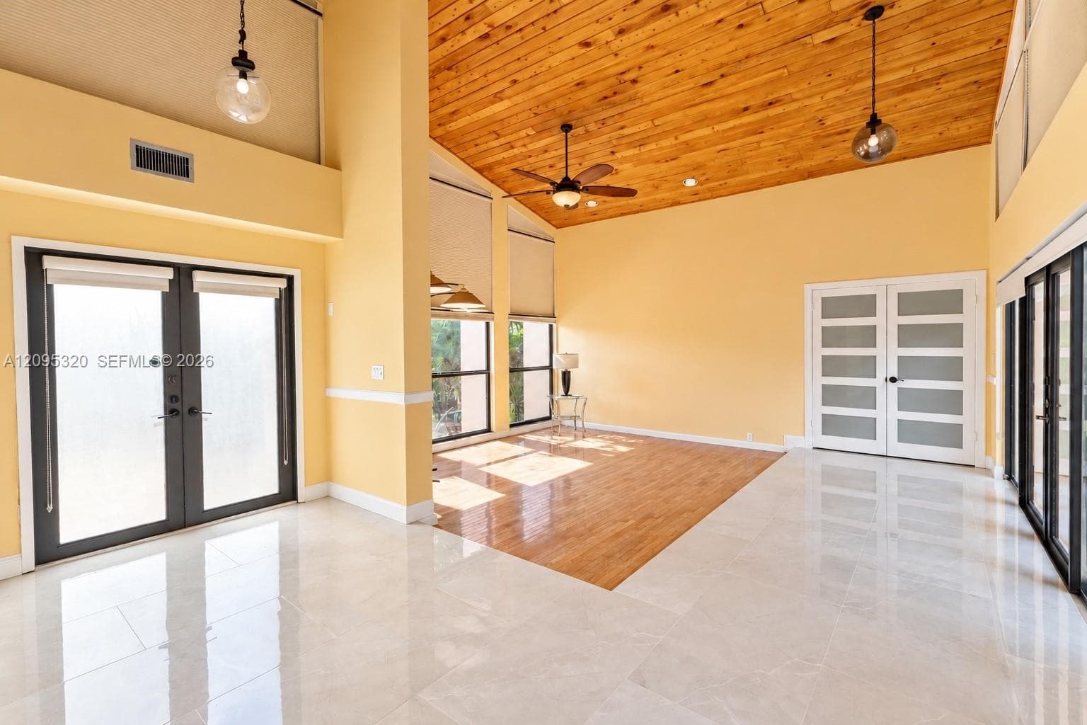 Vaulted wood-plank ceiling, large format tile flooring, wood-finish flooring, two sets of double doors, and multiple windows