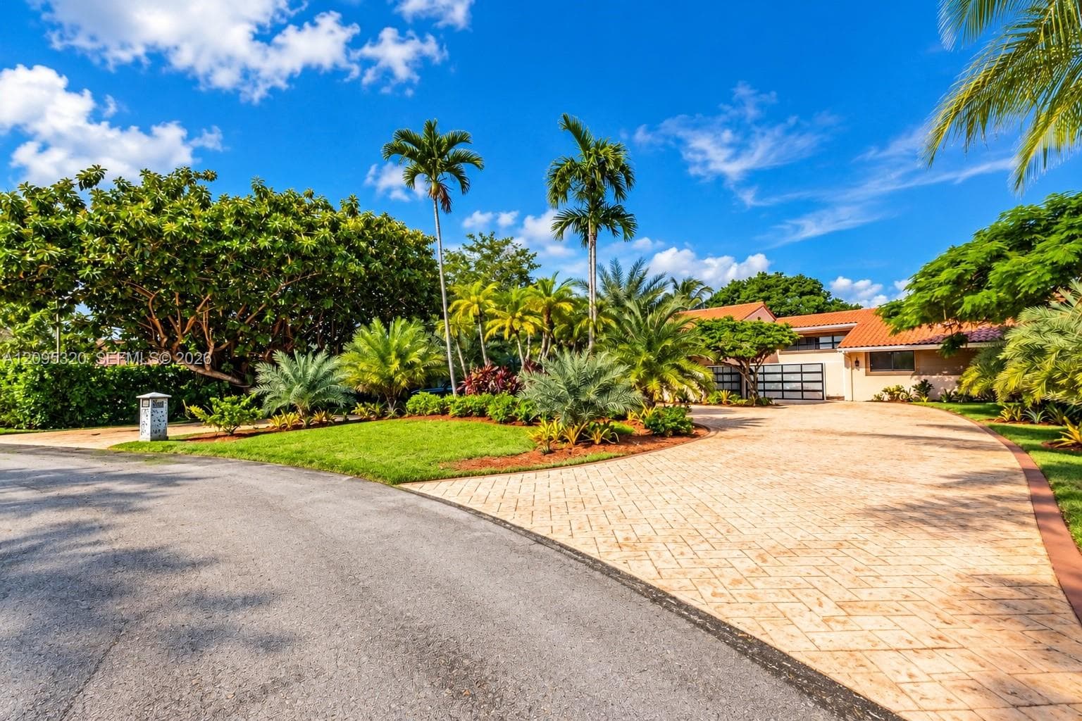Extensive paver driveway with curbing, surrounded by lush landscaping and mature palm trees