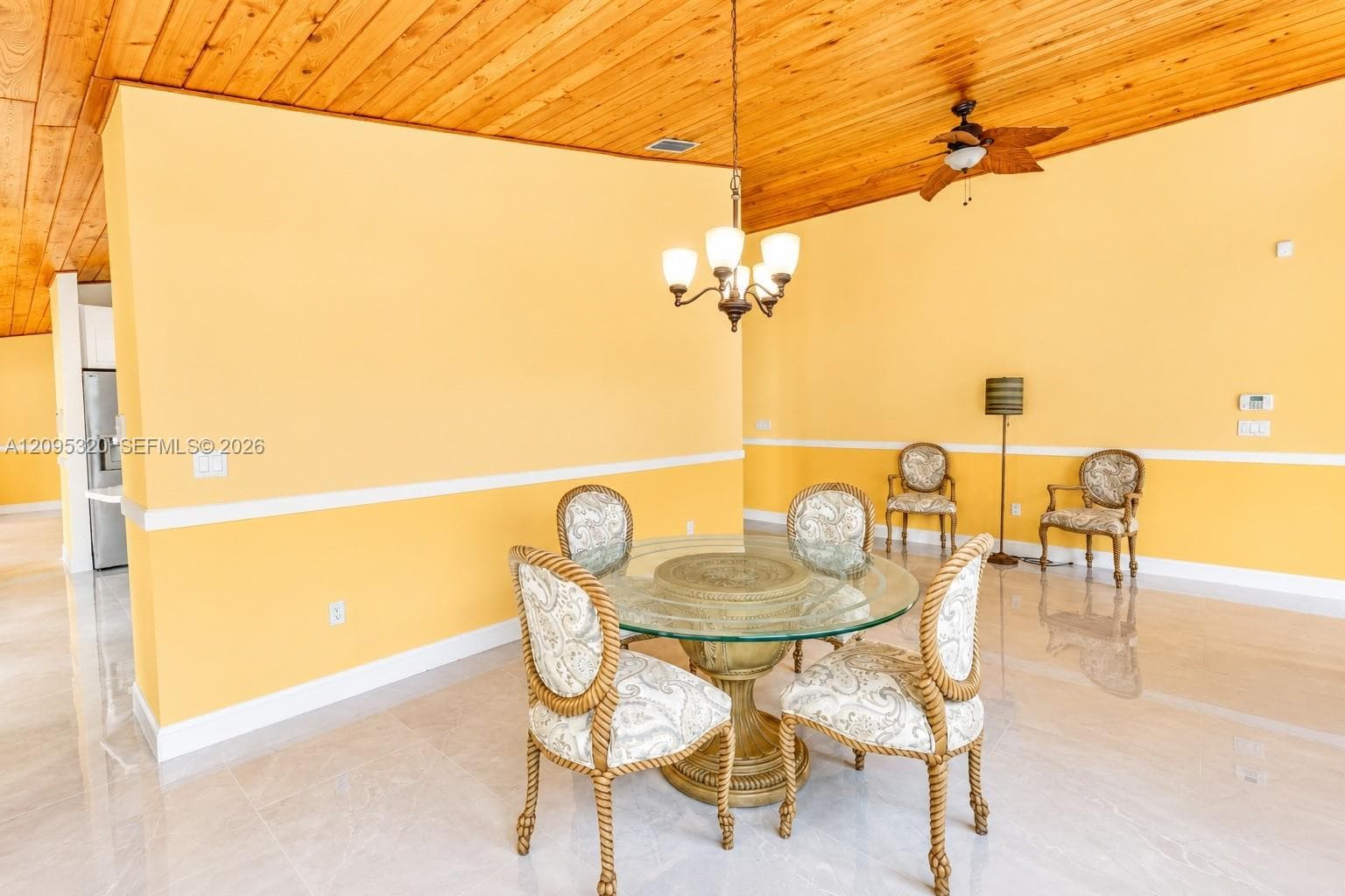 Vaulted wood-paneled ceiling with a ceiling fan, central chandelier, and light-toned flooring
