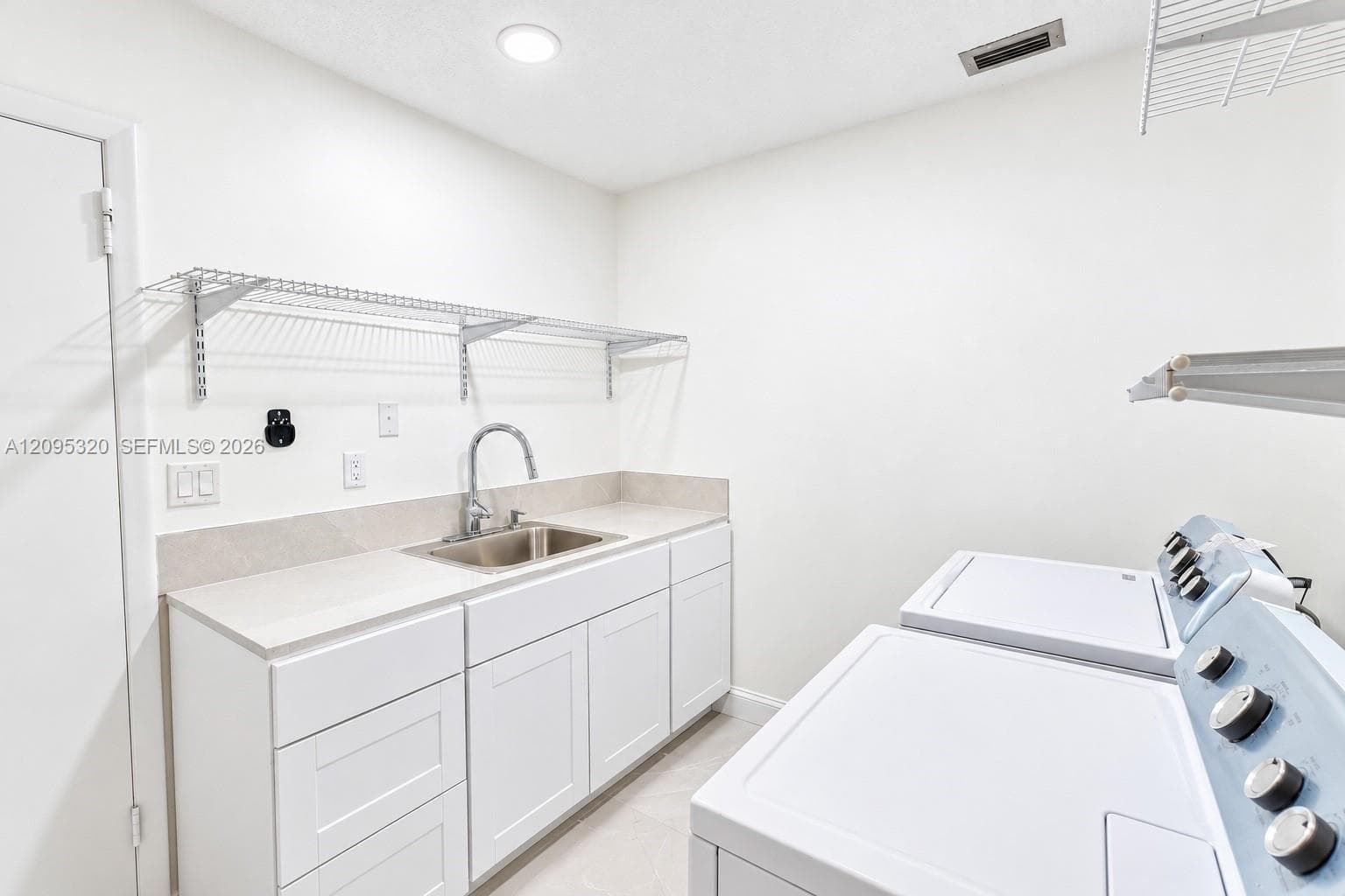 Laundry area featuring white cabinetry, a double basin stainless steel sink, light-toned countertop, and wire shelving