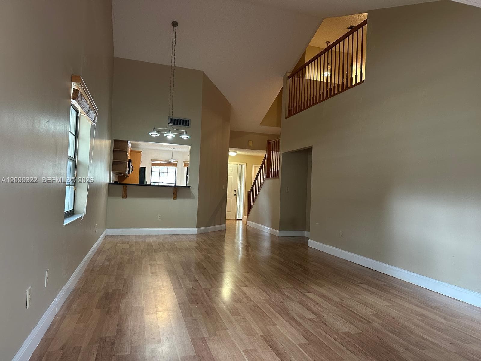Vaulted ceilings, wood-finish flooring, three-light chandelier, pass-through kitchen opening, and wooden stair railing
