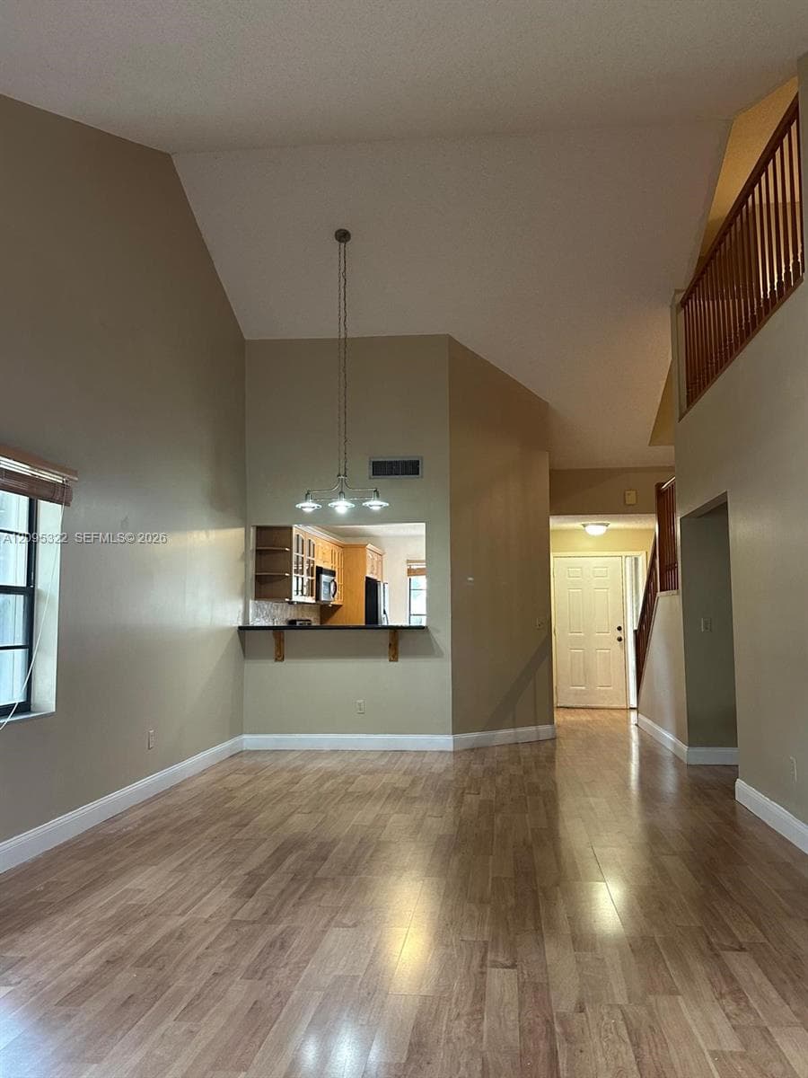 Staircase featuring wood treads and a stained wood railing, complemented by wood-finish flooring and a high-vaulted ceiling