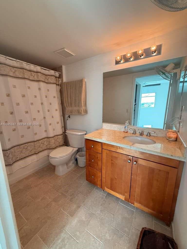 Bathroom featuring wood-finish cabinetry, stone-surface countertop with an integrated basin, large vanity mirror, and ceramic tile flooring