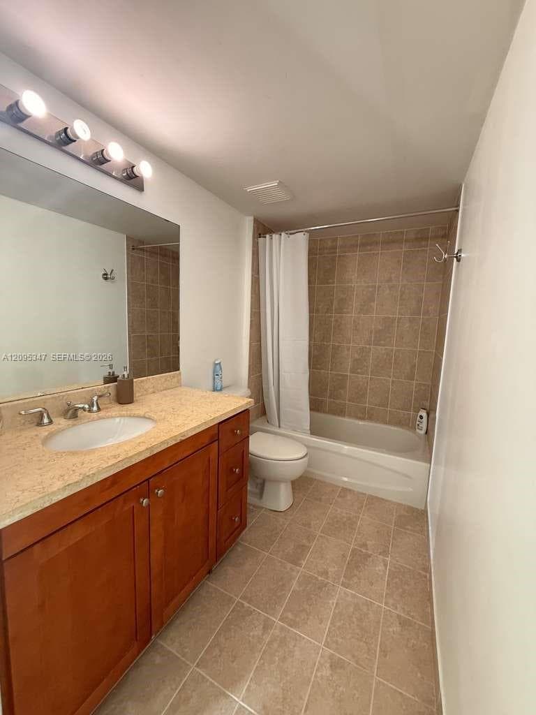 Bathroom featuring wood-finish cabinetry, stone-texture countertop, integrated porcelain sink, tiled tub surround, and ceramic tile flooring