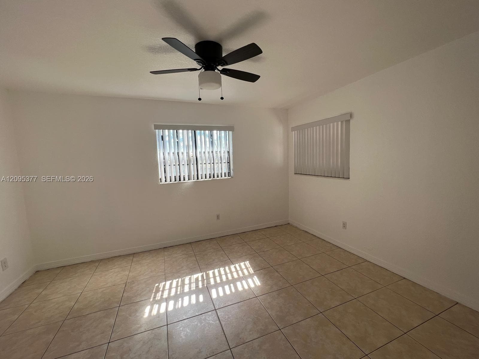Neutral wall tones, ceramic tile flooring, matte black ceiling fan with integrated lighting, and vertical window blinds