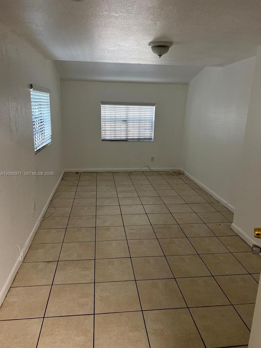 Interior room featuring large-format ceramic tile flooring, neutral wall finishes, and two windows equipped with horizontal blinds, illuminated by a flush-mount ceiling fixture
