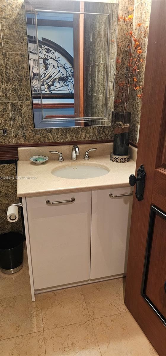 Vanity with a solid surface countertop, integrated oval basin, polished chrome widespread faucet, white cabinetry with horizontal hardware, and a beveled-edge wall mirror set against tiled walls