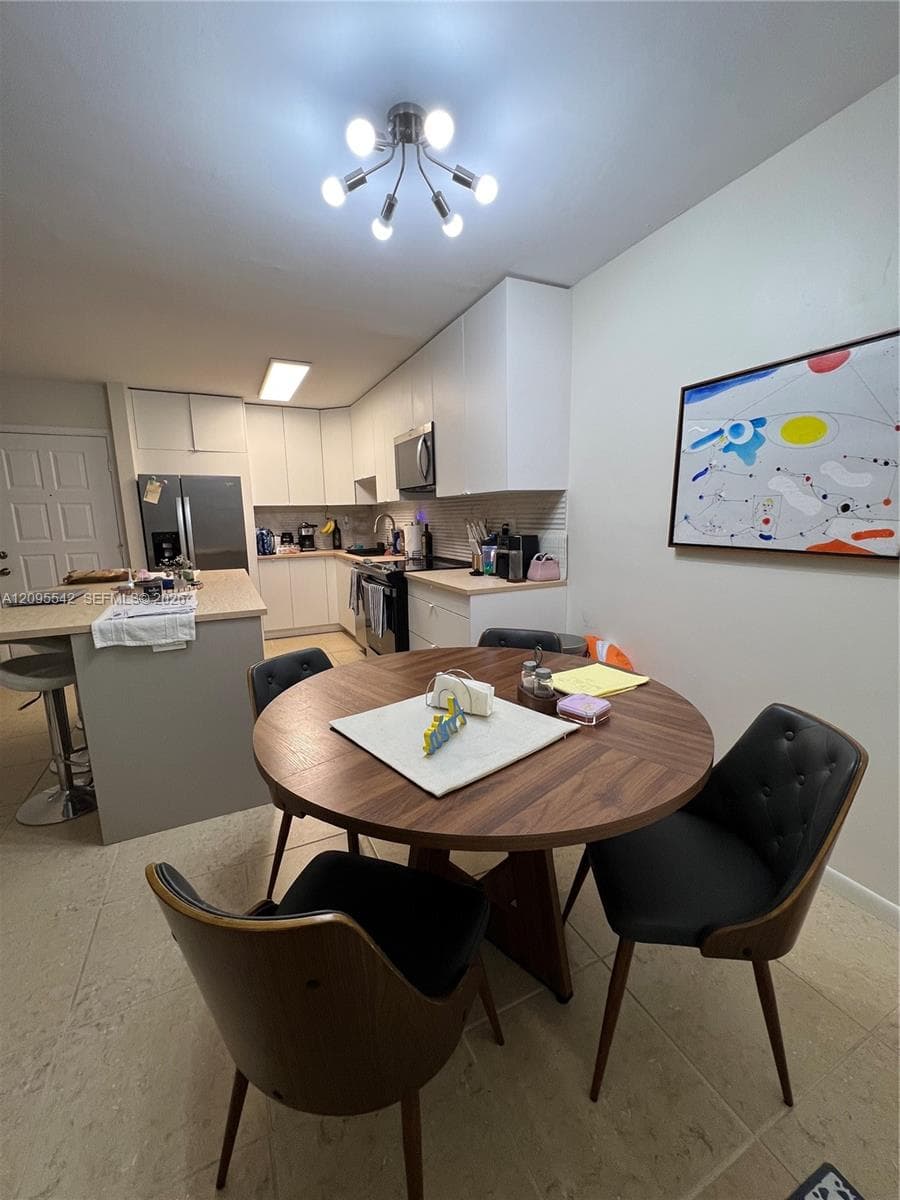 Kitchen featuring flat-panel white cabinetry, a center island with countertop seating, stone-style tile flooring, and a multi-arm modern light fixture