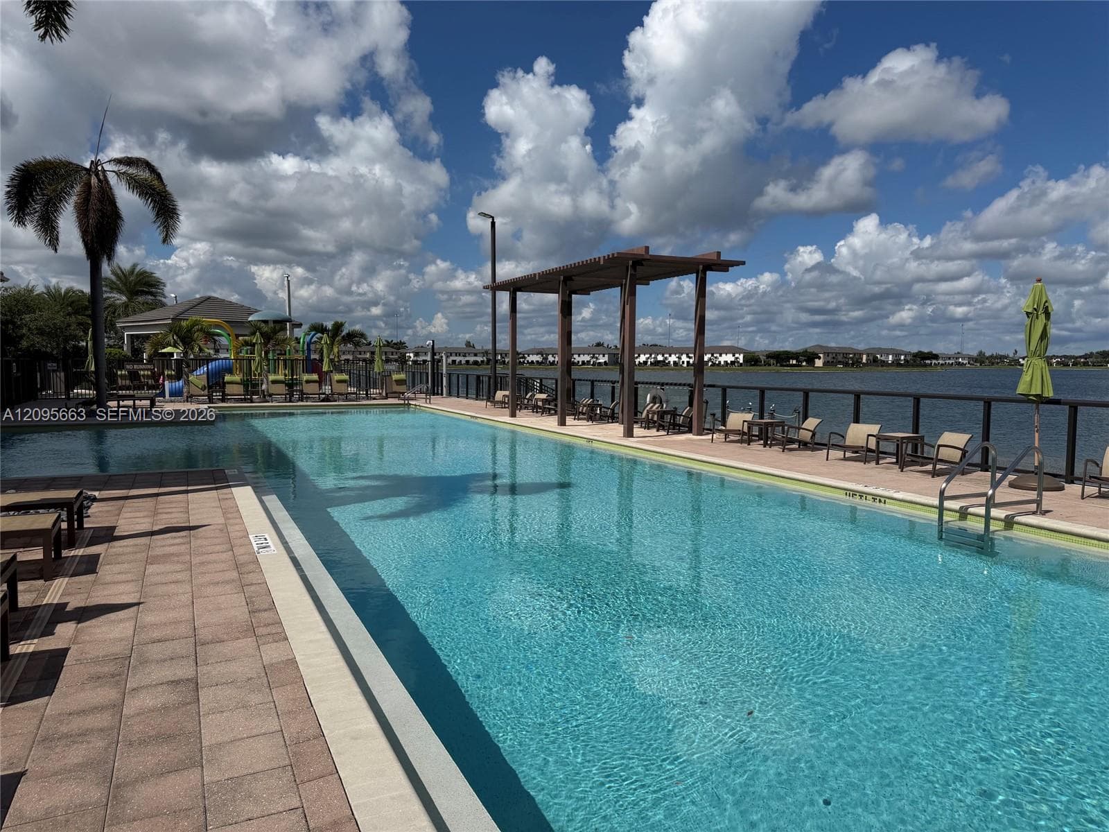 Swimming pool with paver decking, pergola structure, metal perimeter fencing, and water frontage