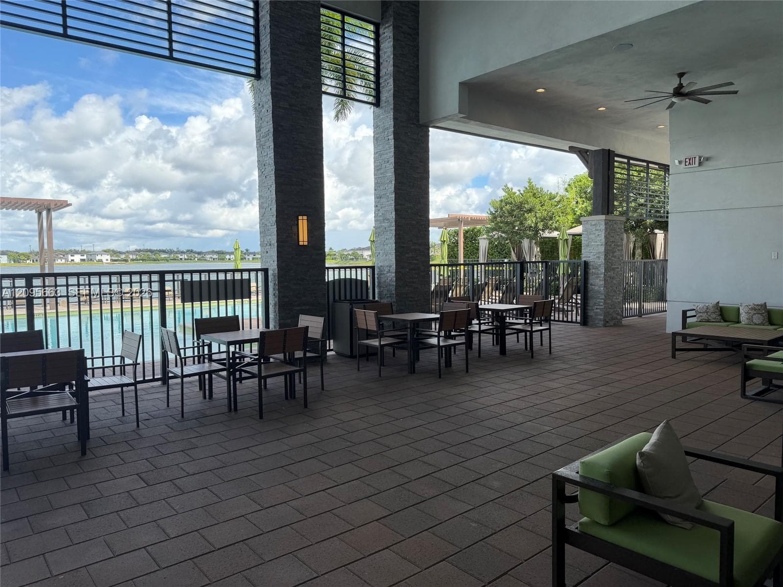 Covered outdoor terrace featuring stone-clad structural pillars, large-format paver flooring, recessed ceiling lighting, and overhead ceiling fans