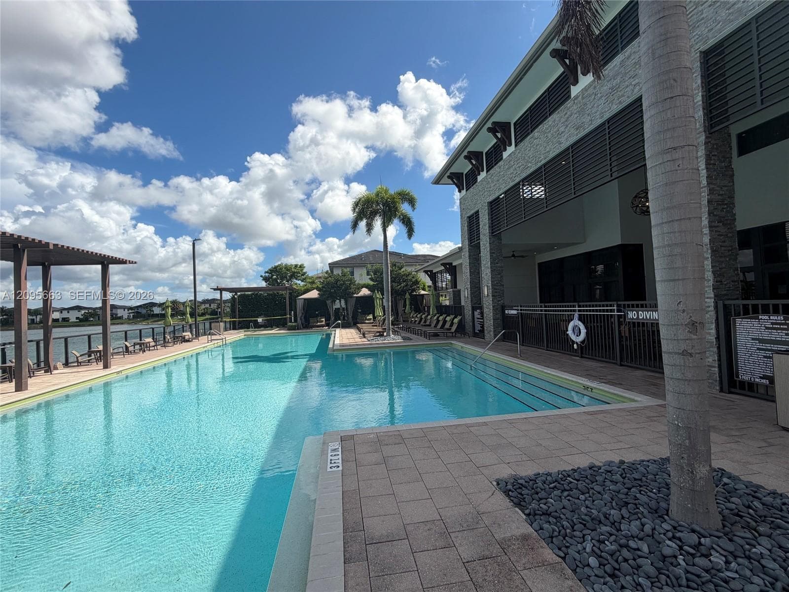 Resort-style swimming pool featuring a tanning ledge, stone paver decking, pergola-covered seating, and custom rock landscaping accents
