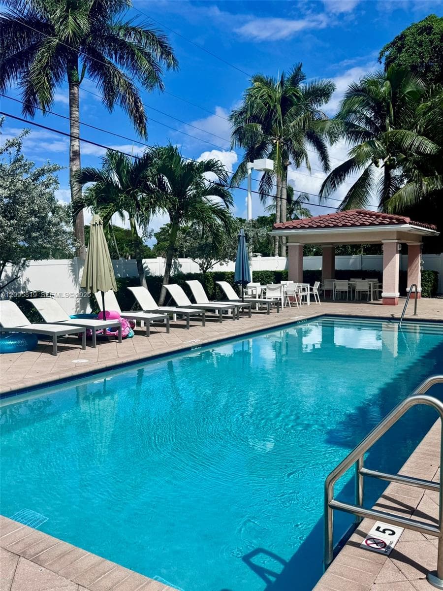 In-ground swimming pool featuring a tiled deck, stainless steel handrails, and a covered pavilion with a terracotta-style roof