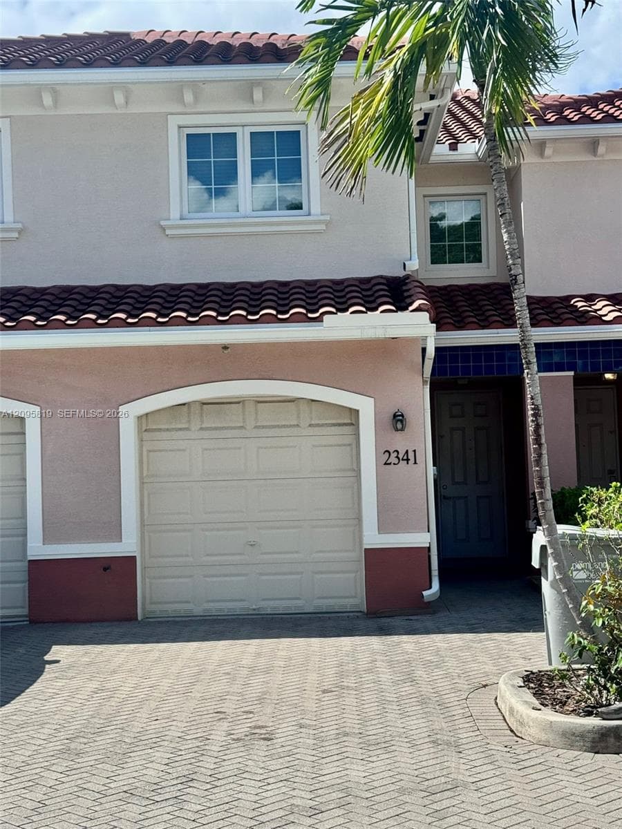 Stucco exterior featuring a terracotta tile roof, arched garage entry, multi-pane windows, and a paved driveway