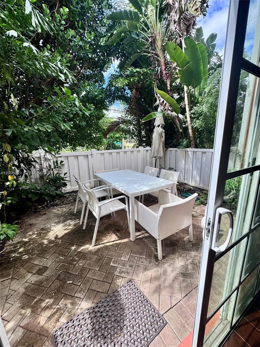 Enclosed patio featuring herringbone-patterned stone pavers, white privacy fencing, and established mature landscaping