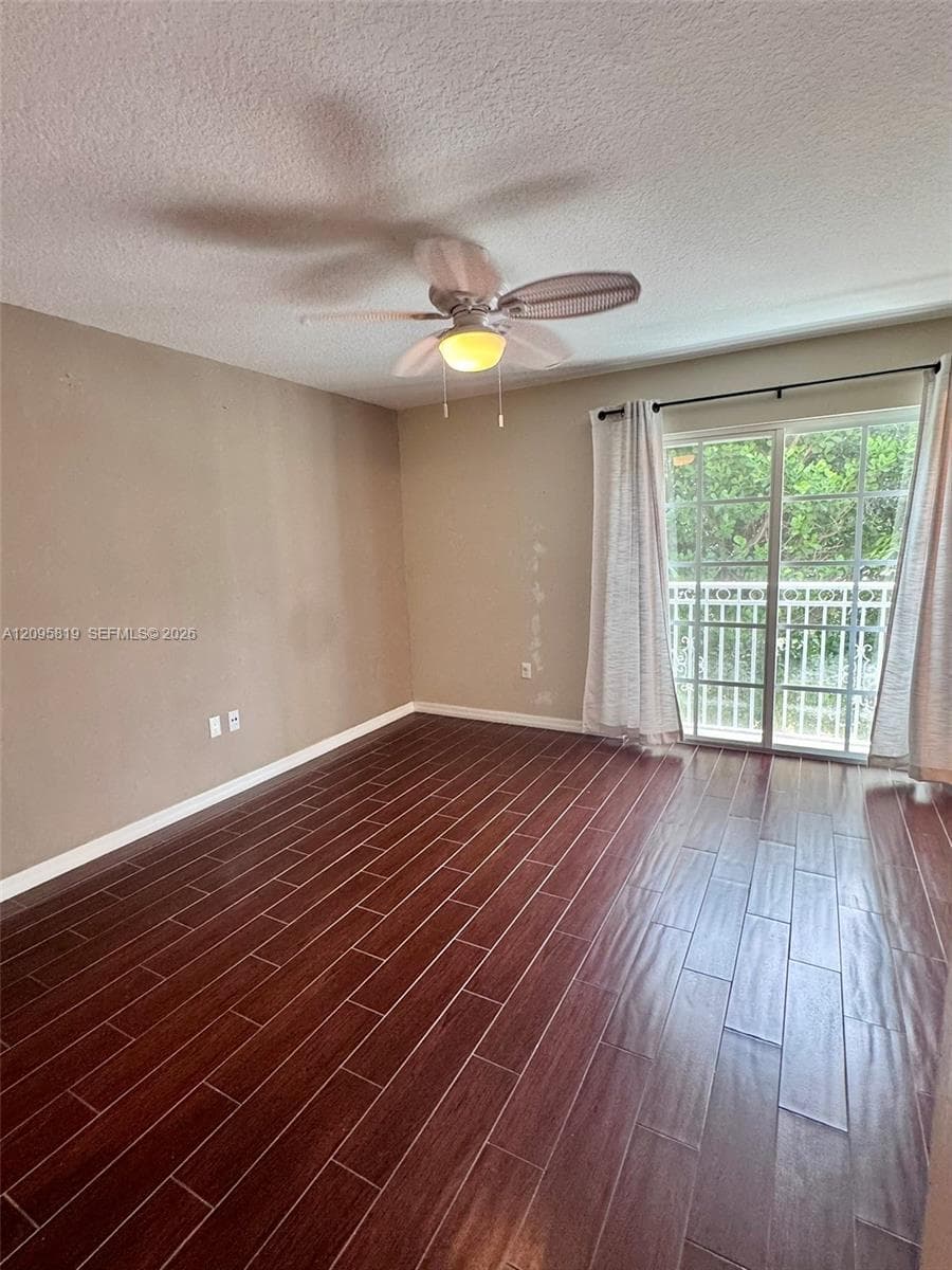 Interior room featuring wood-finish tile flooring, a ceiling fan with integrated light fixture, and glass sliding doors with access to an exterior balcony