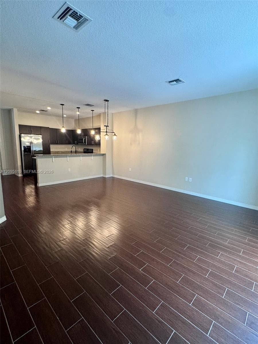 Open-concept area featuring wood-finish flooring, dark cabinetry, a breakfast bar, and multiple pendant light fixtures
