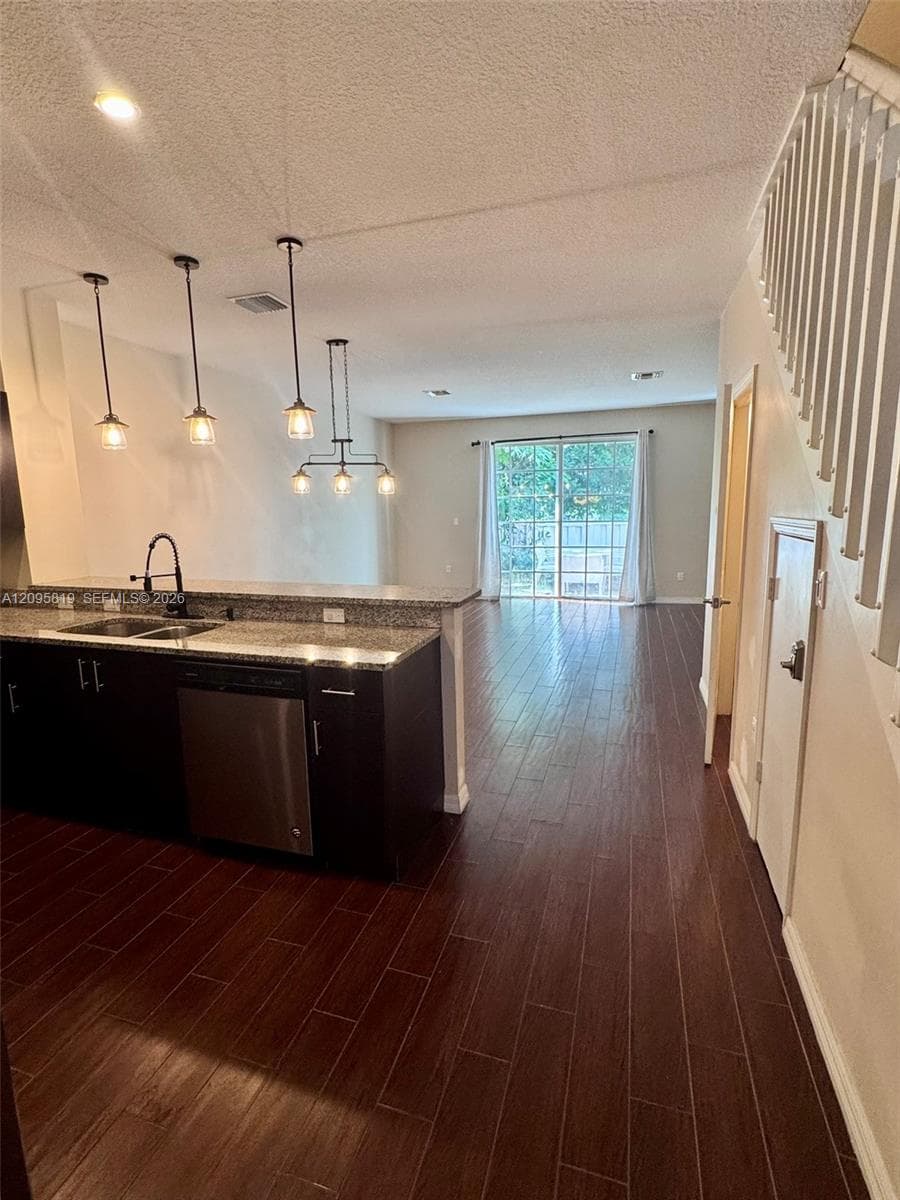 Kitchen featuring dark cabinetry, stone-surface countertops, a double-basin stainless steel sink with a matte black faucet, wood-finish tile flooring, and multi-pendant lighting
