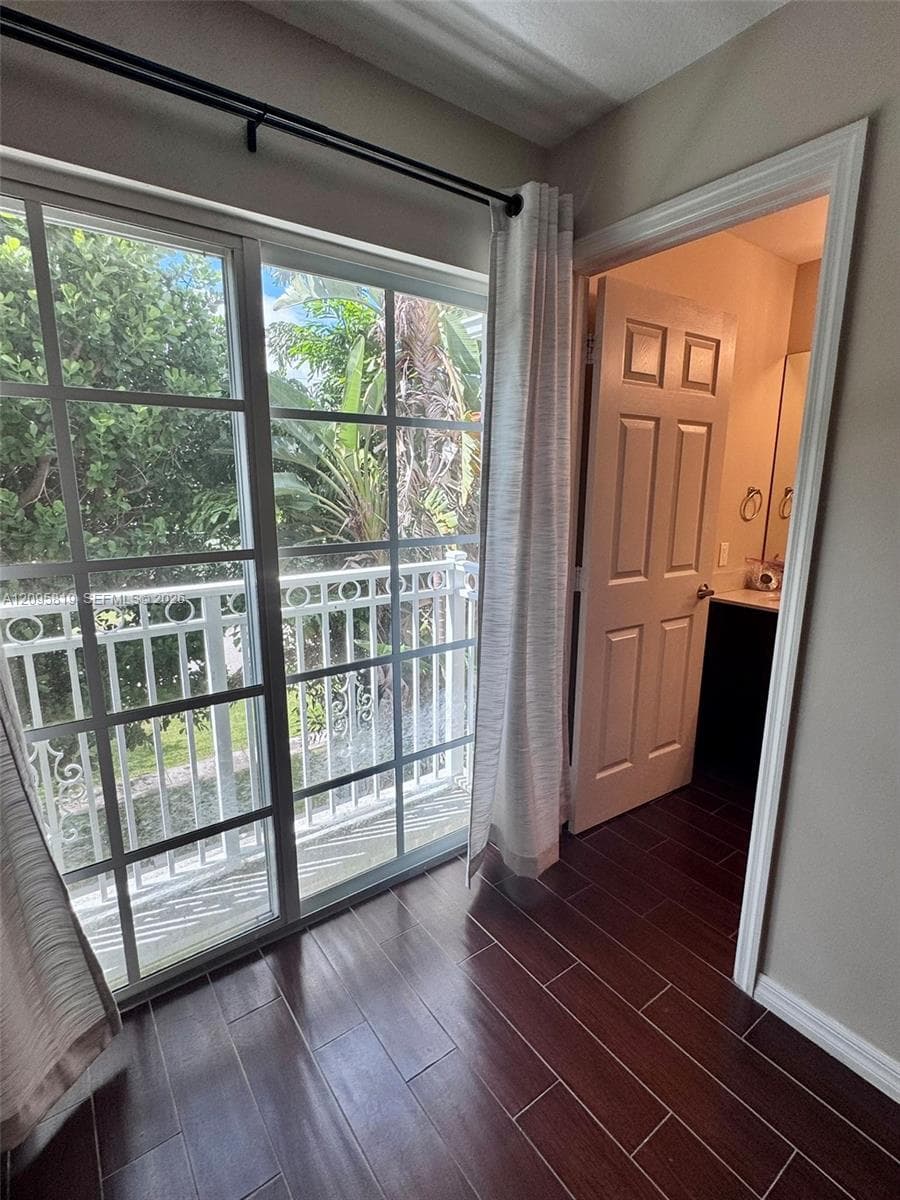 Sliding glass doors with grid detailing, wood-finish tile flooring, and a private balcony with decorative railing
