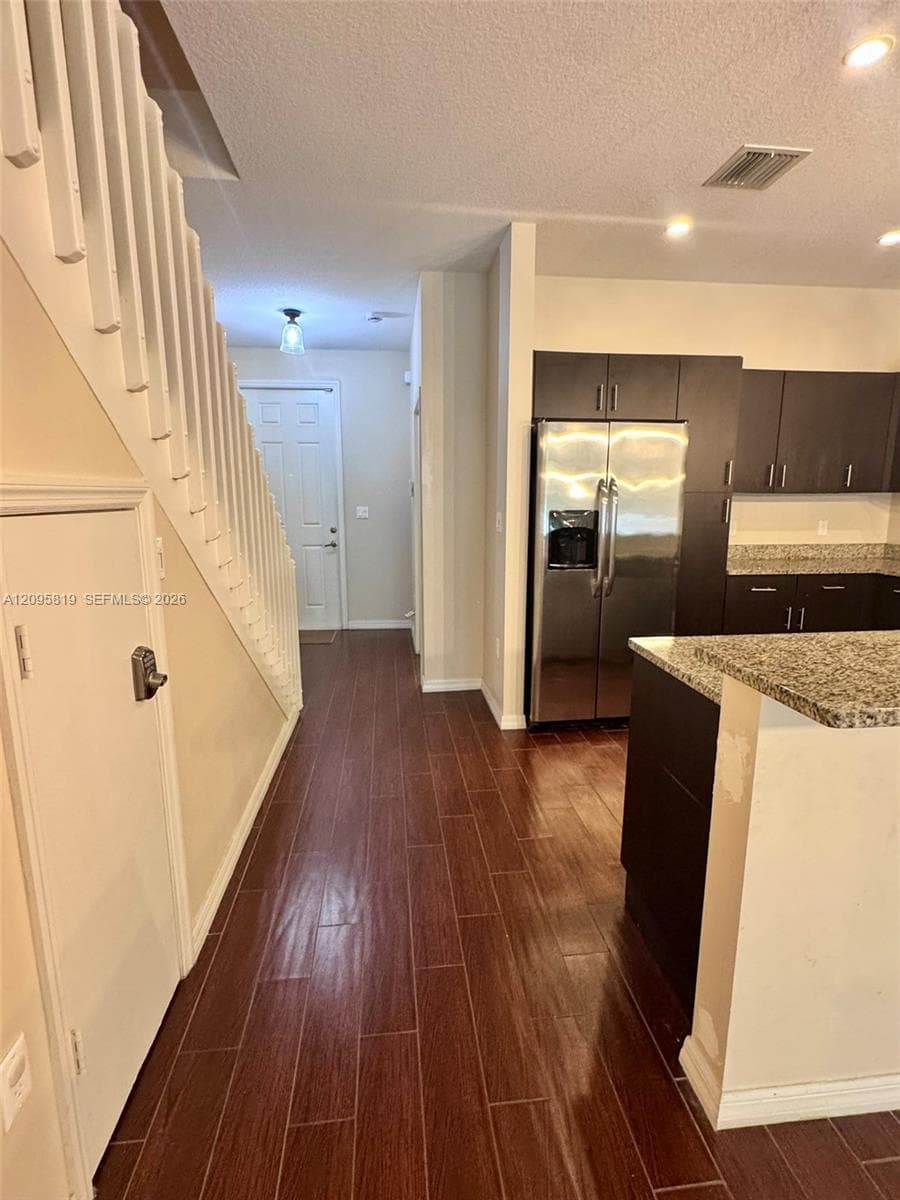 Dark wood-finish plank flooring, stainless steel side-by-side refrigerator, flat-panel cabinetry, stone-finish countertops, and white staircase with vertical balusters