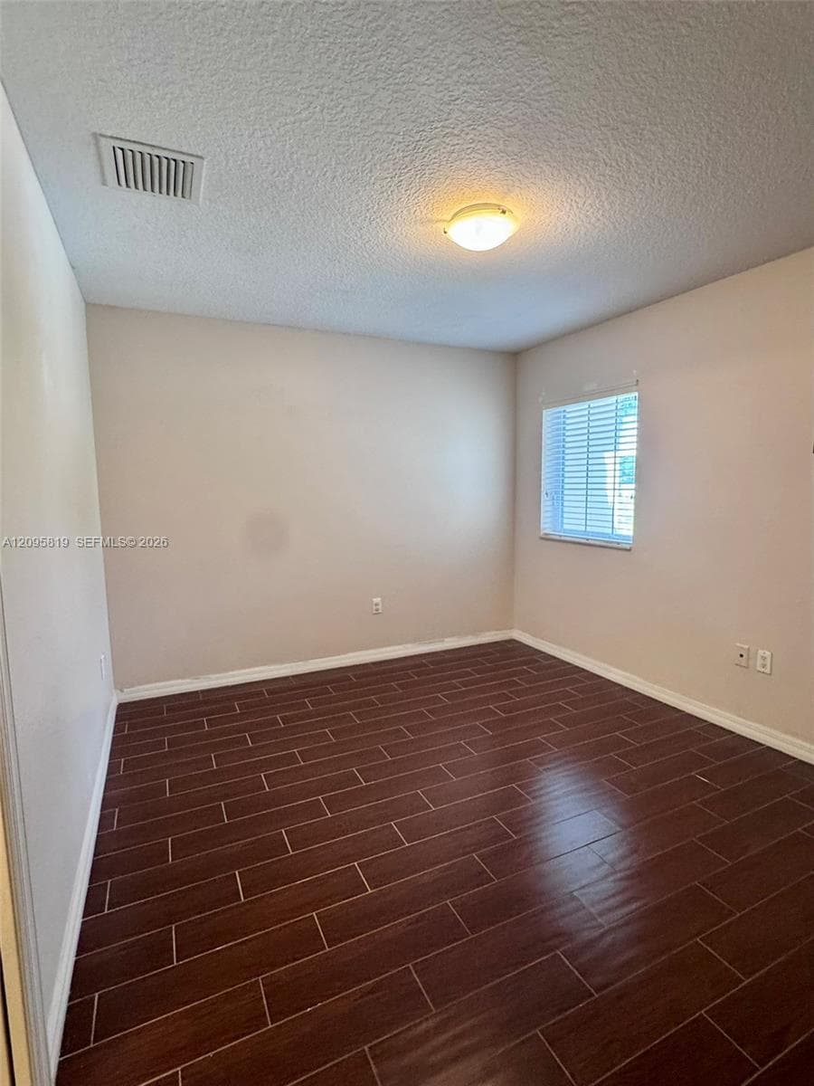 Neutral-toned interior space featuring dark wood-finish flooring, a single-pane window with installed horizontal blinds, and a flush-mount ceiling fixture